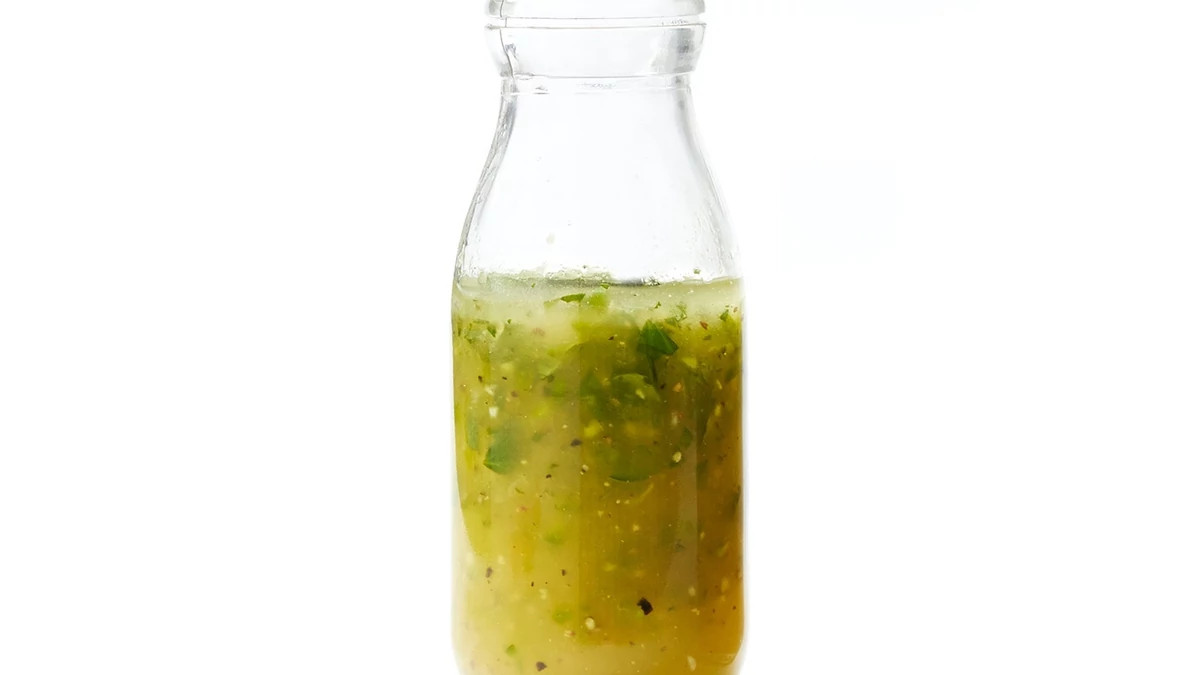 A close-up view of citrus-lime vinaigrette in a glass on a white background
