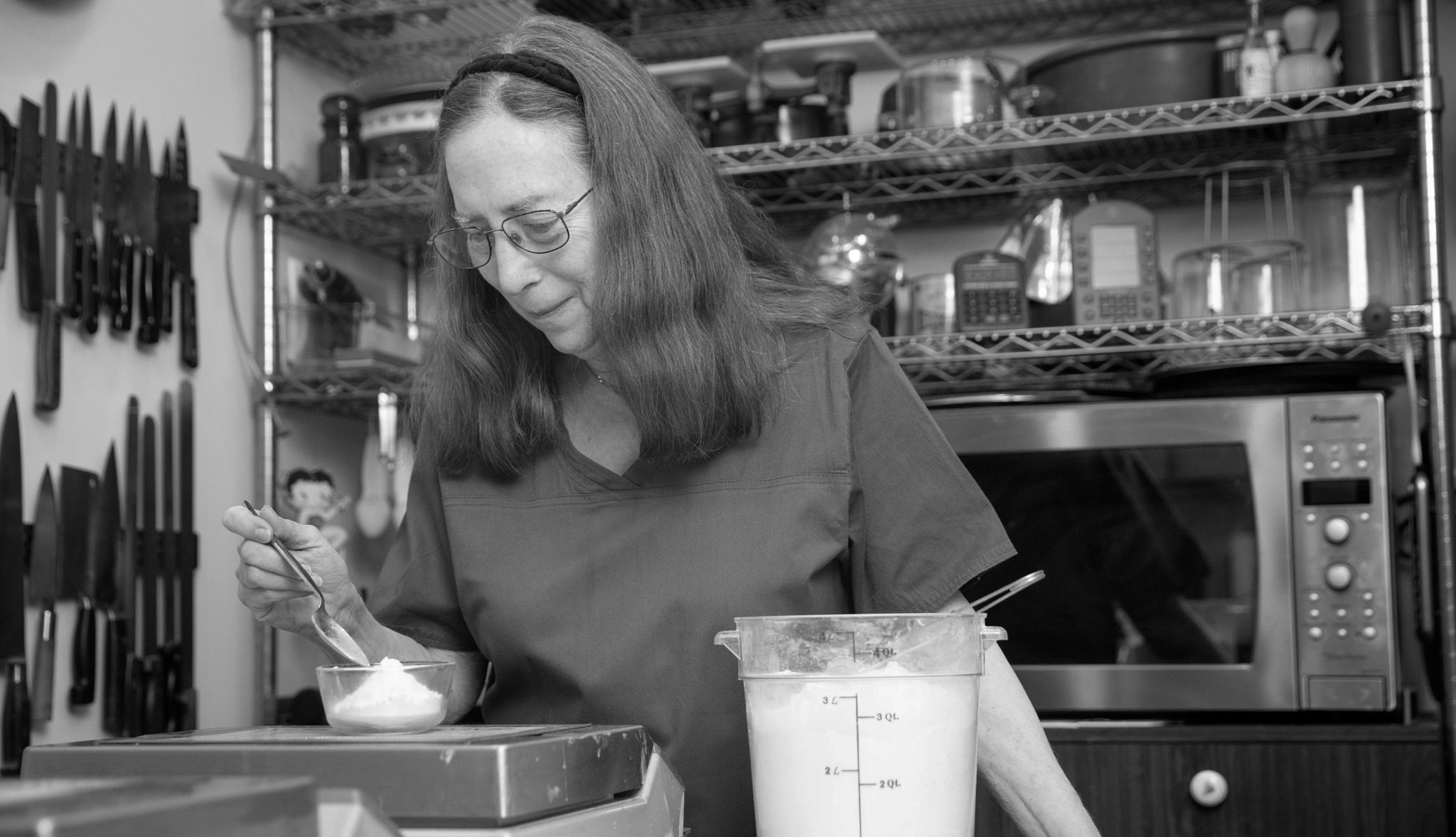 Rose Levy Beranbaum in a kitchen Rose Levy Beranbaum in a kitchen, mixing powder in a bowl, microwave and kitchen supplies behind her