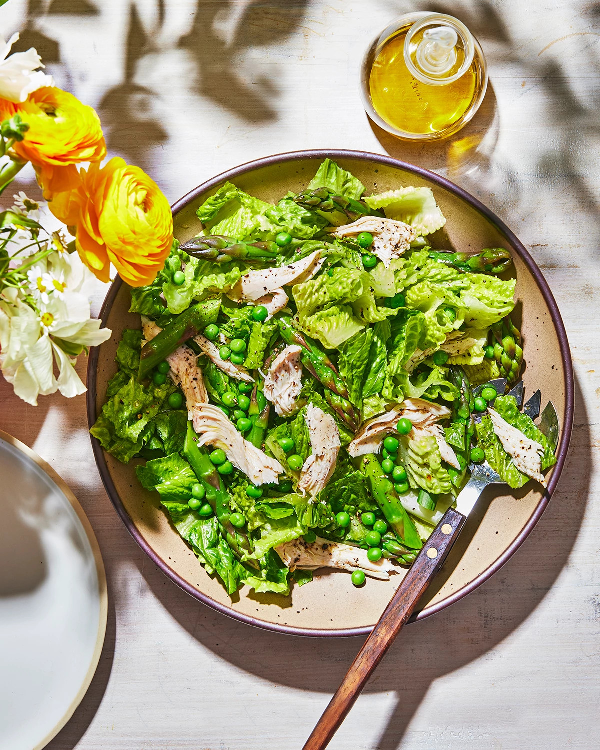 A vibrant plate of shredded chicken salad styled on a sunlit table with flowers and olive oil
