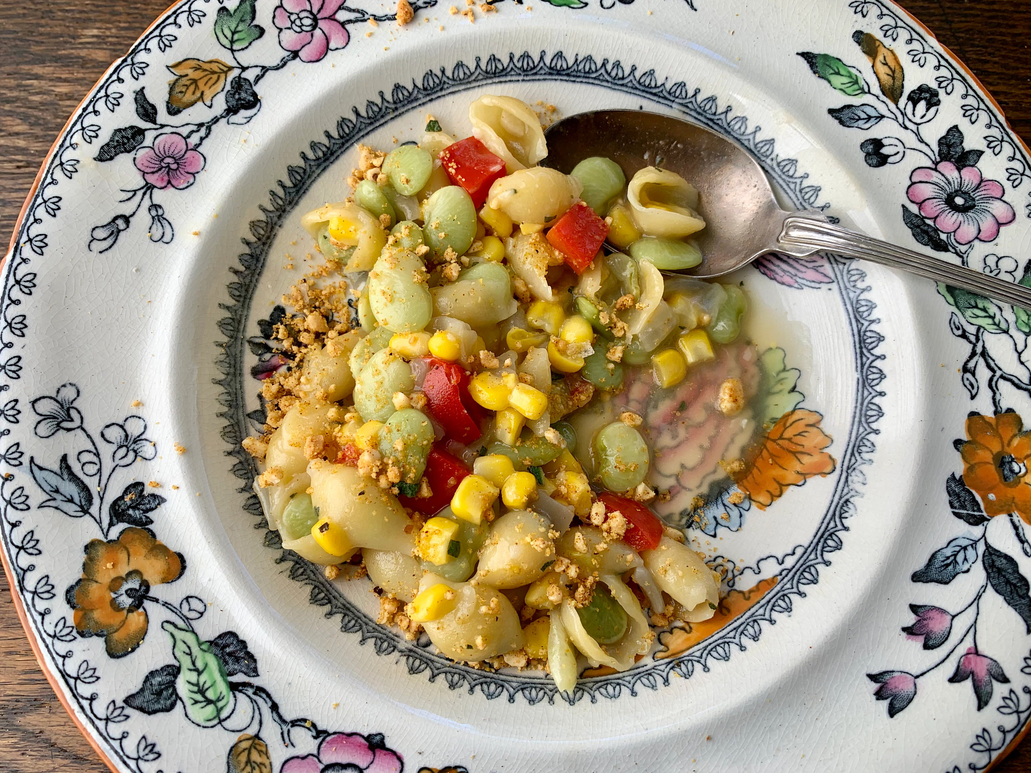Succotash and Shells with lima beans, corn and cut up red bell peppers in dish with spoon in it