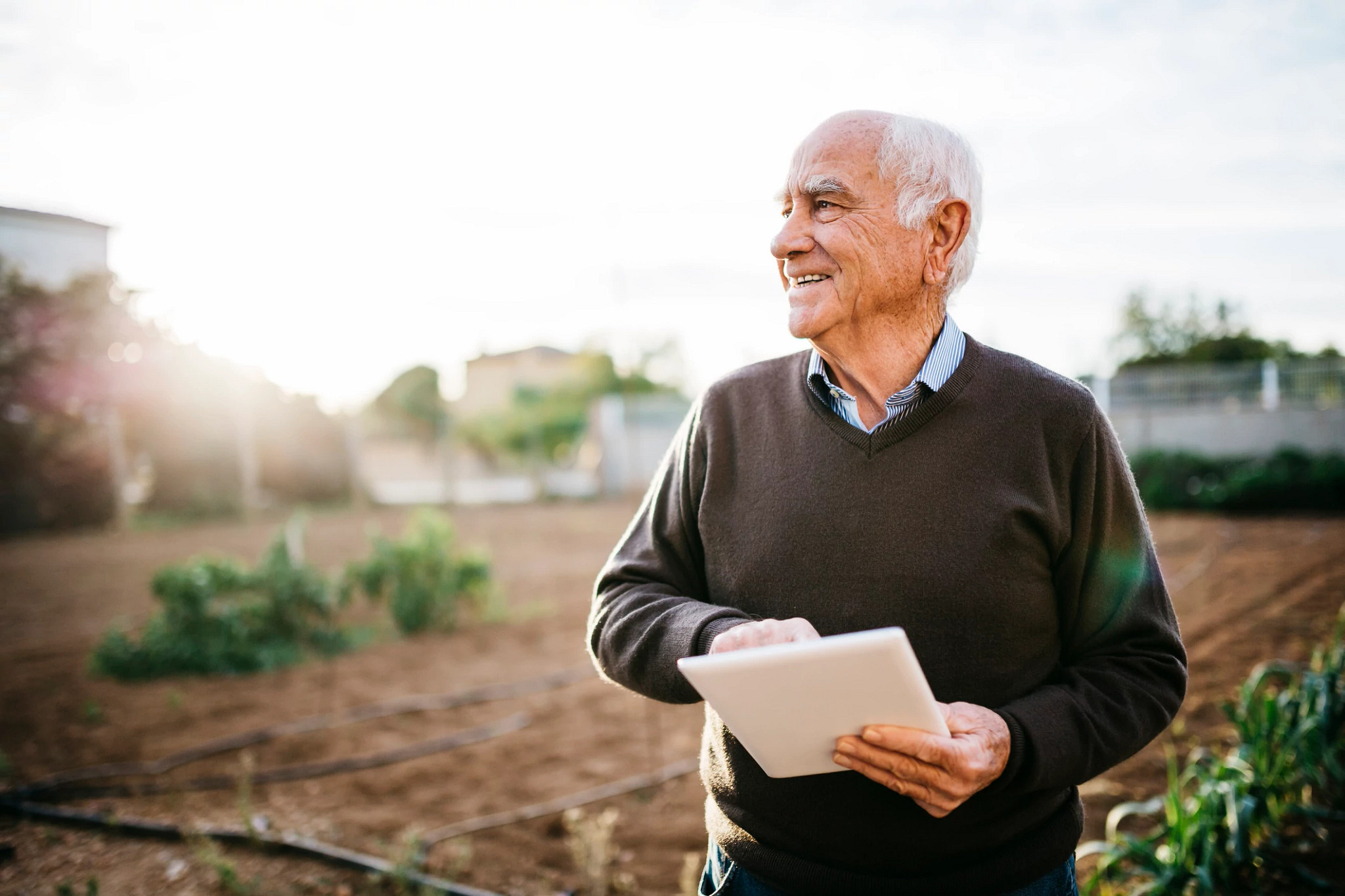 Older man smiling with an iPad in his garden