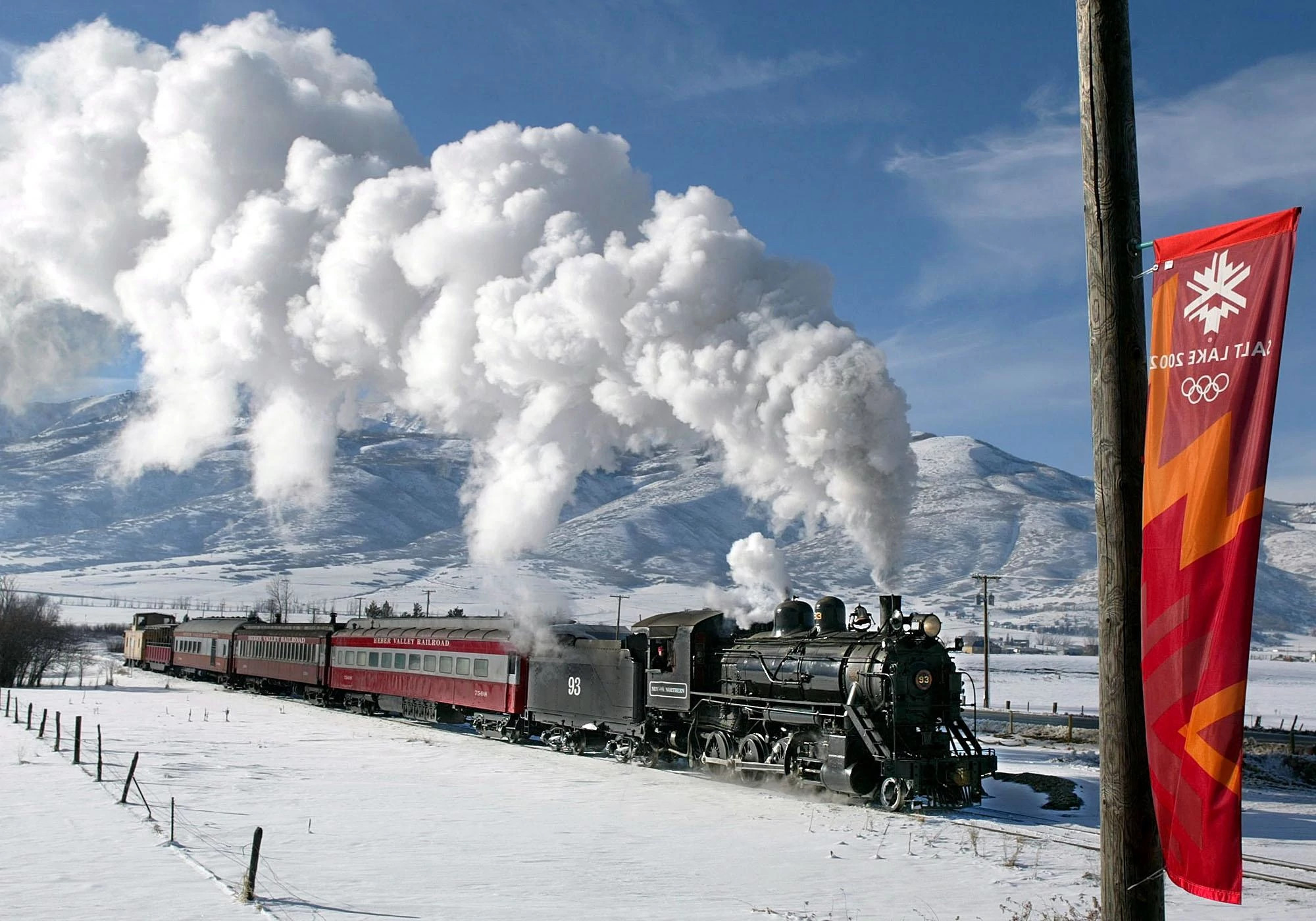 a train with a smoke plume traveling through a snow covered mountain area