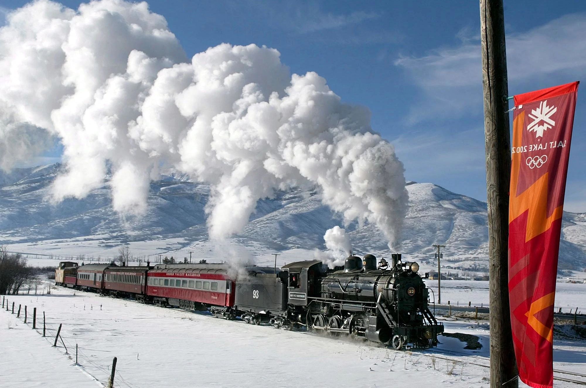 a train with a smoke plume traveling through a snow covered mountain area