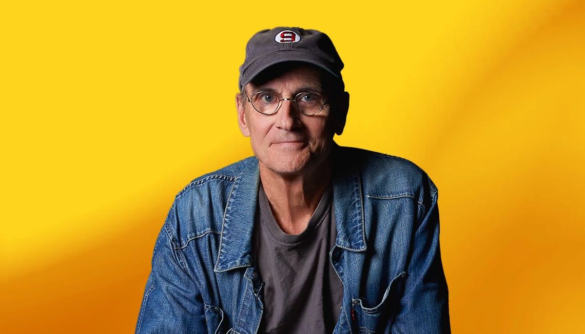 James Taylor interview James Taylor wearing jean jacket and hat with number nine on it, against yellow ombre background