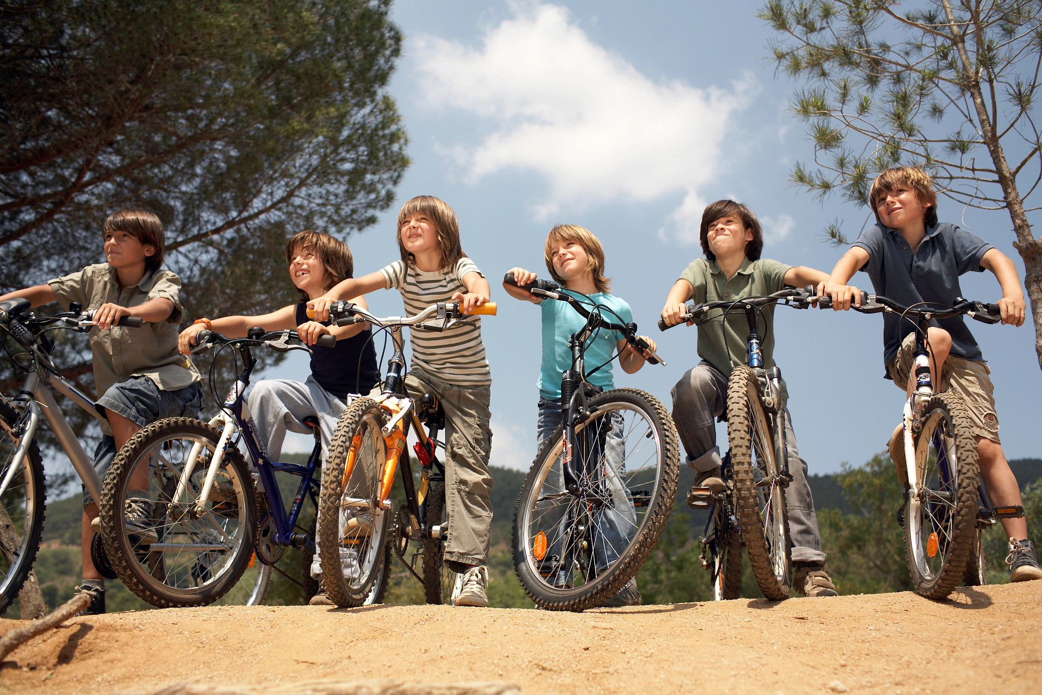 a photo shows a group of preteen boys on their bicycles, ready to ride down a dirt hill