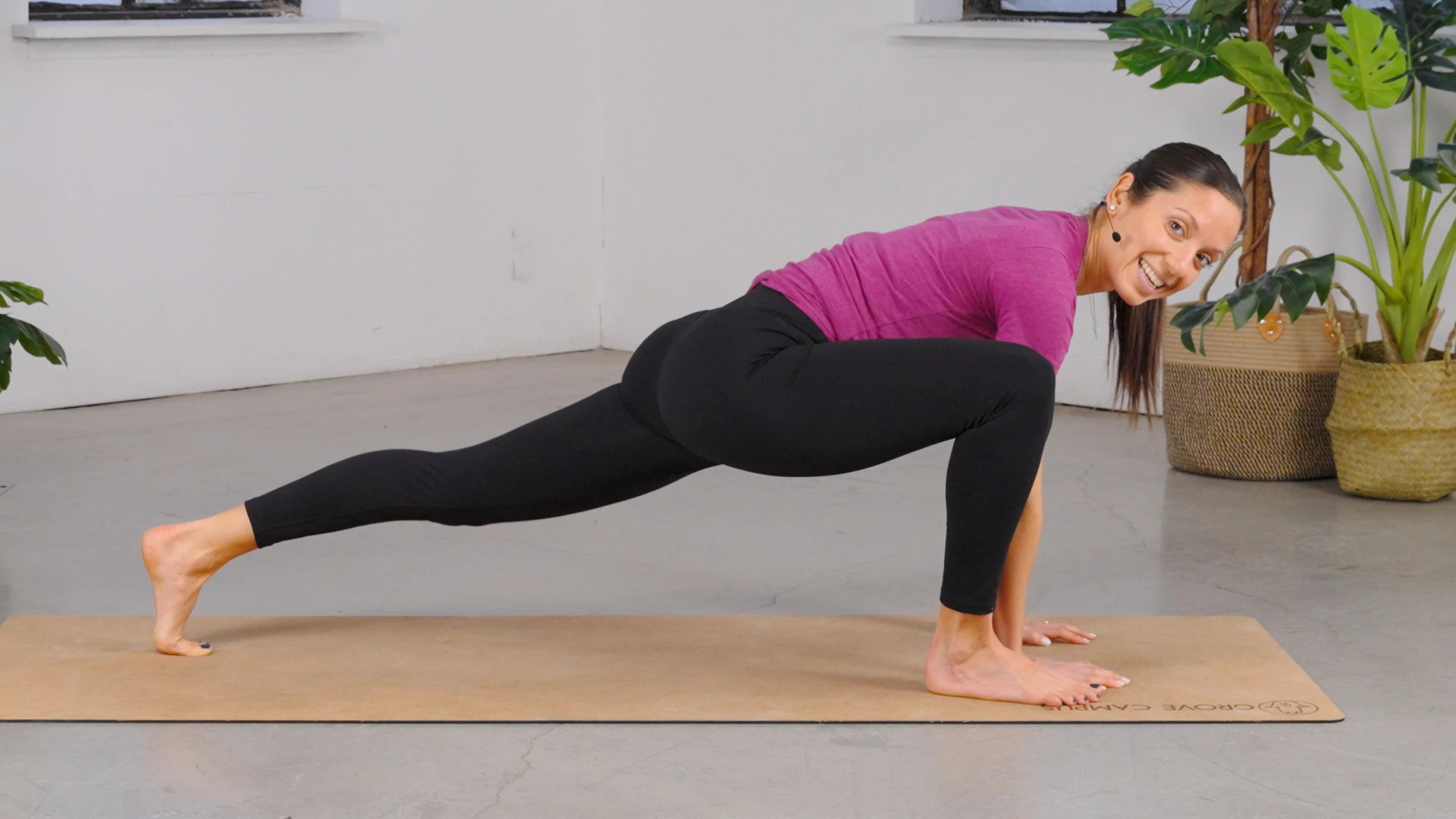 Sideview of Niki Pislis on mat, lunging forward with right leg bent in front and left leg straight back, hands in front of her on mat