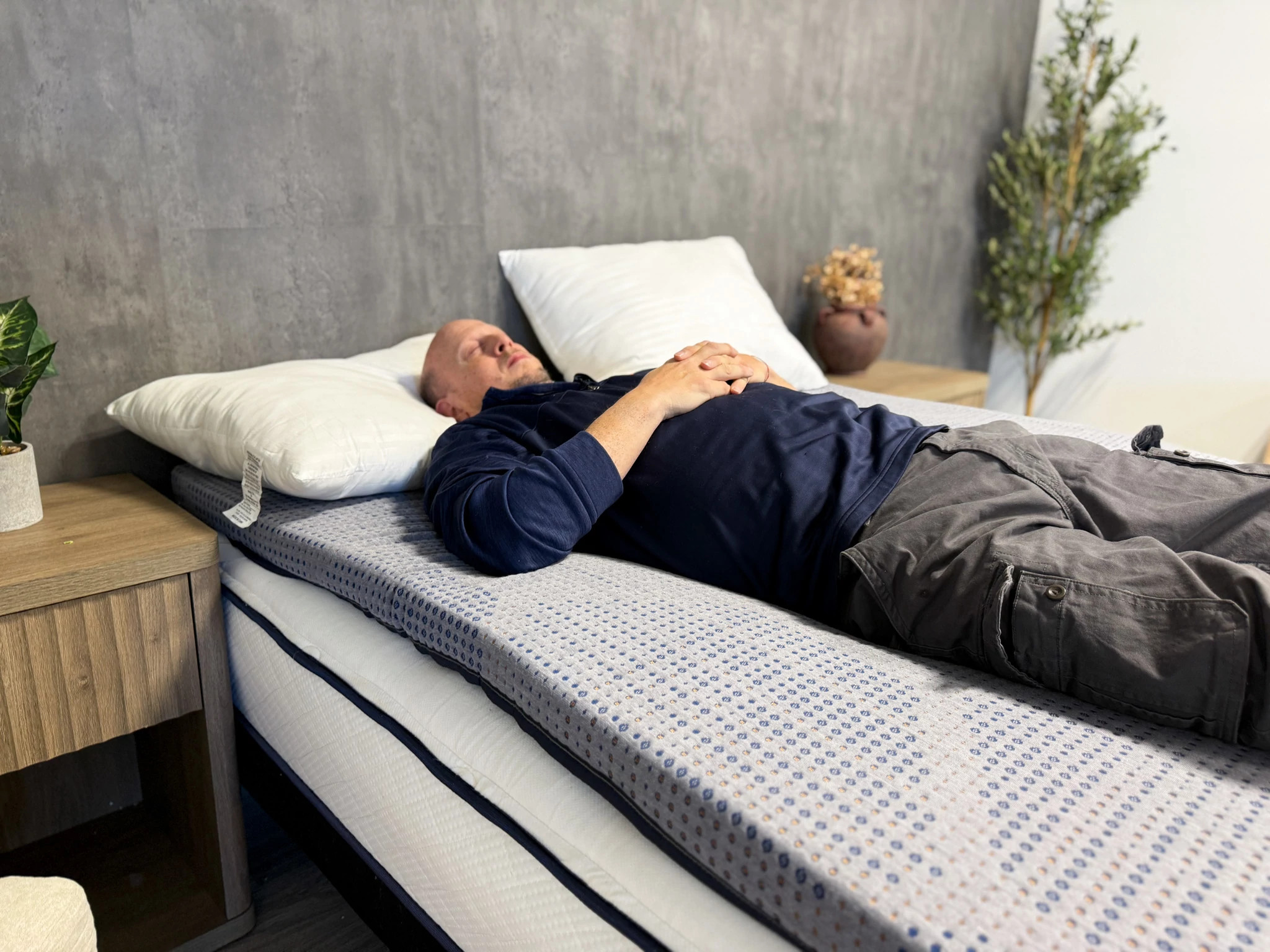 Man lies on his back in bed with his eyes closed and hands clasped on his stomach