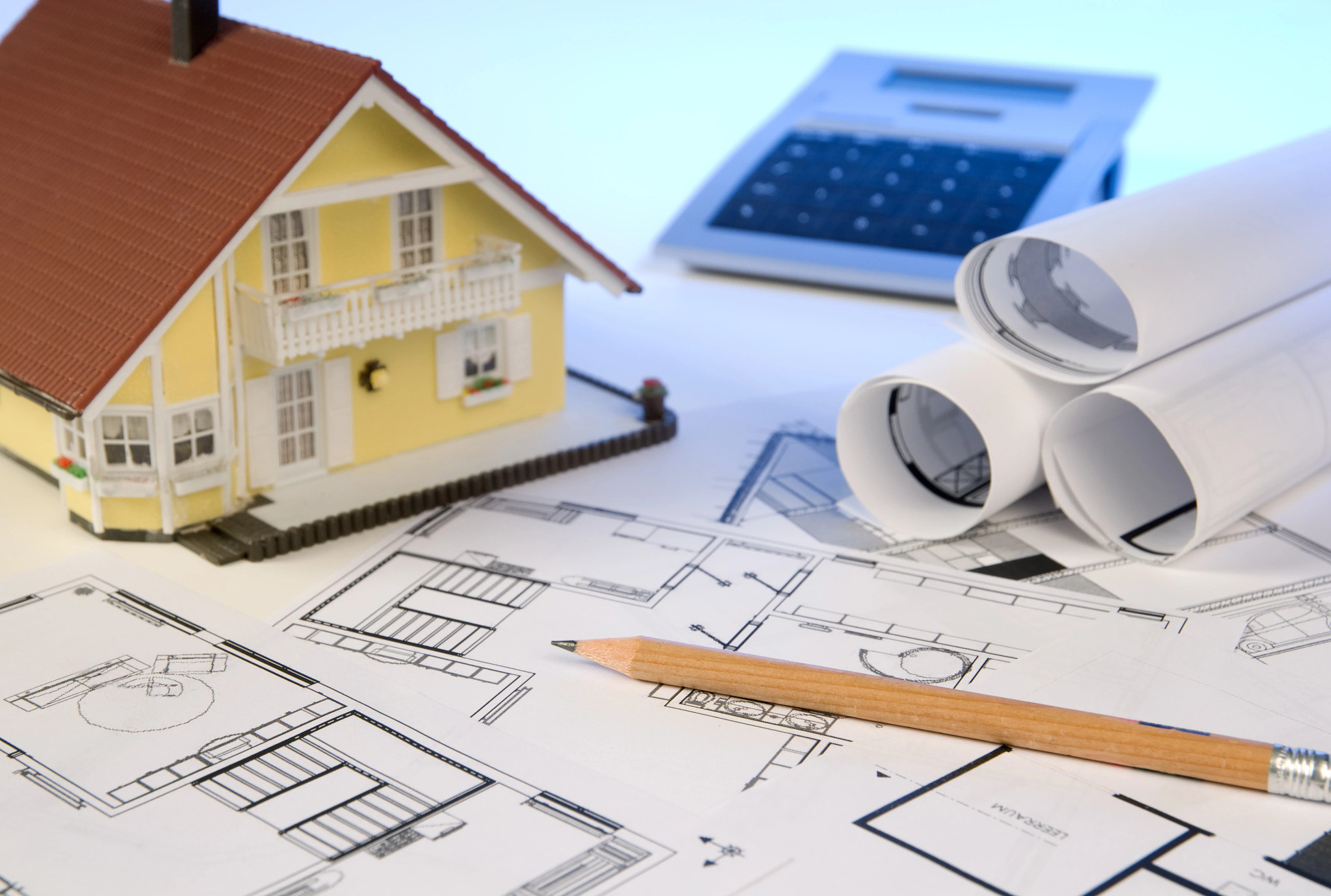 a small model home sitting on a stack of house plans with a calculator in the background