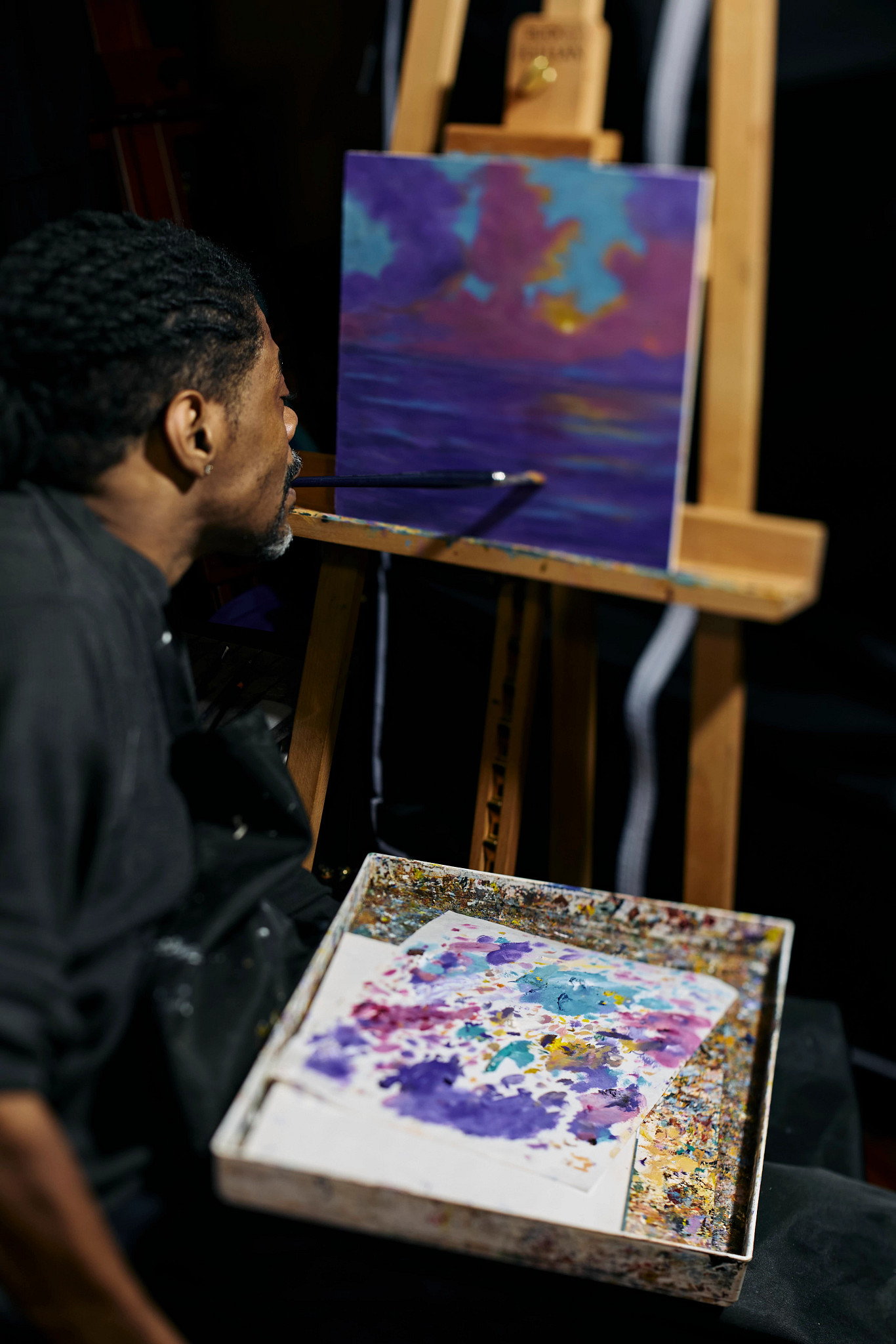 antonio davis using his mouth to hold a paintbrush while working on a painting on an easel