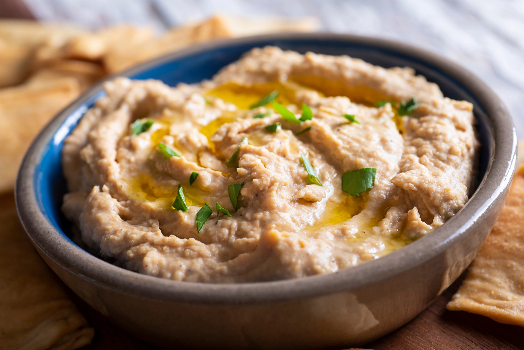 Close-up of creamy bean dip topped with olive oil and fresh herbs, served with crackers