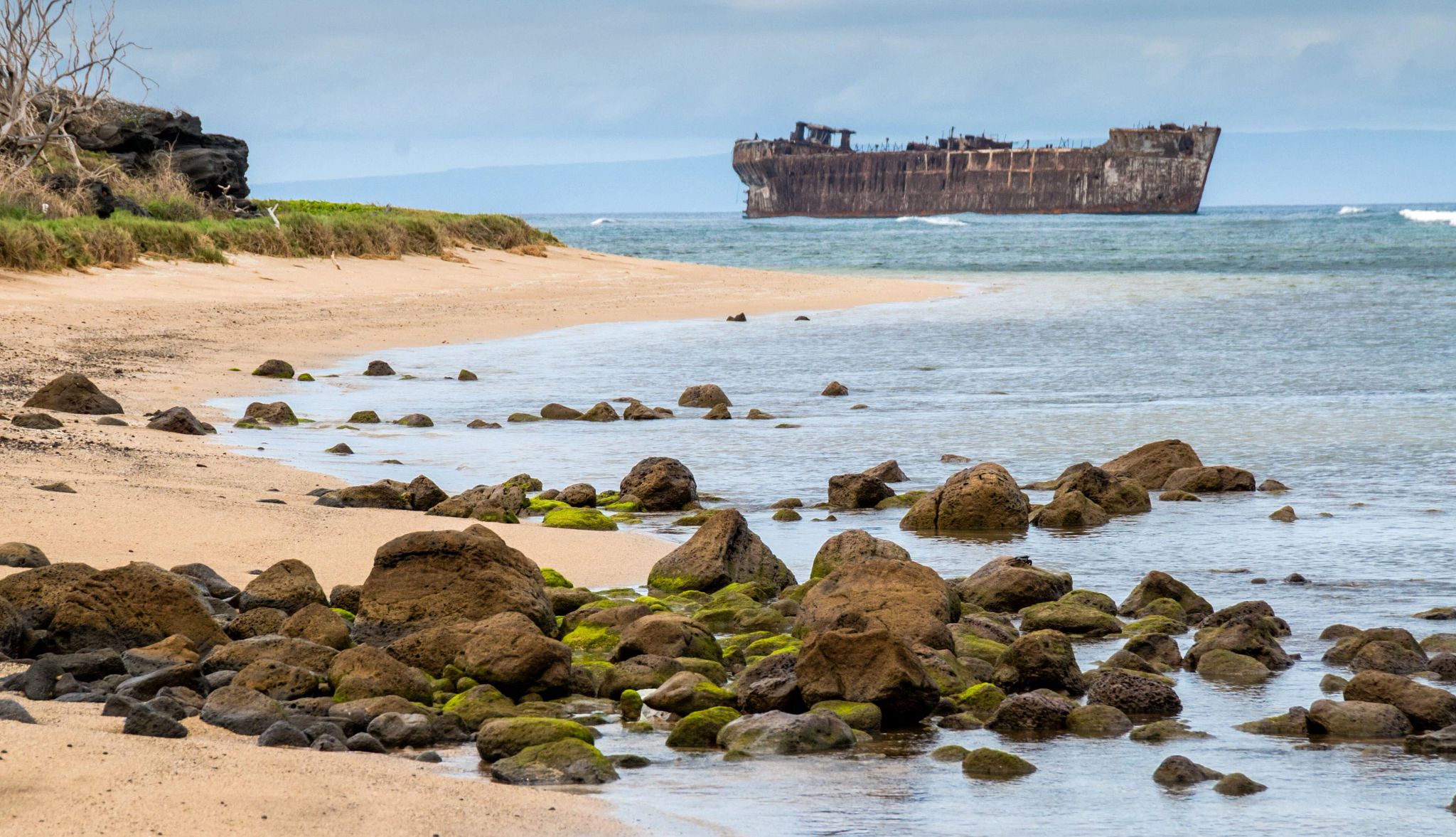 America's Hidden Beaches rocks covered in moss at a beach with a shipwreck in the beackground