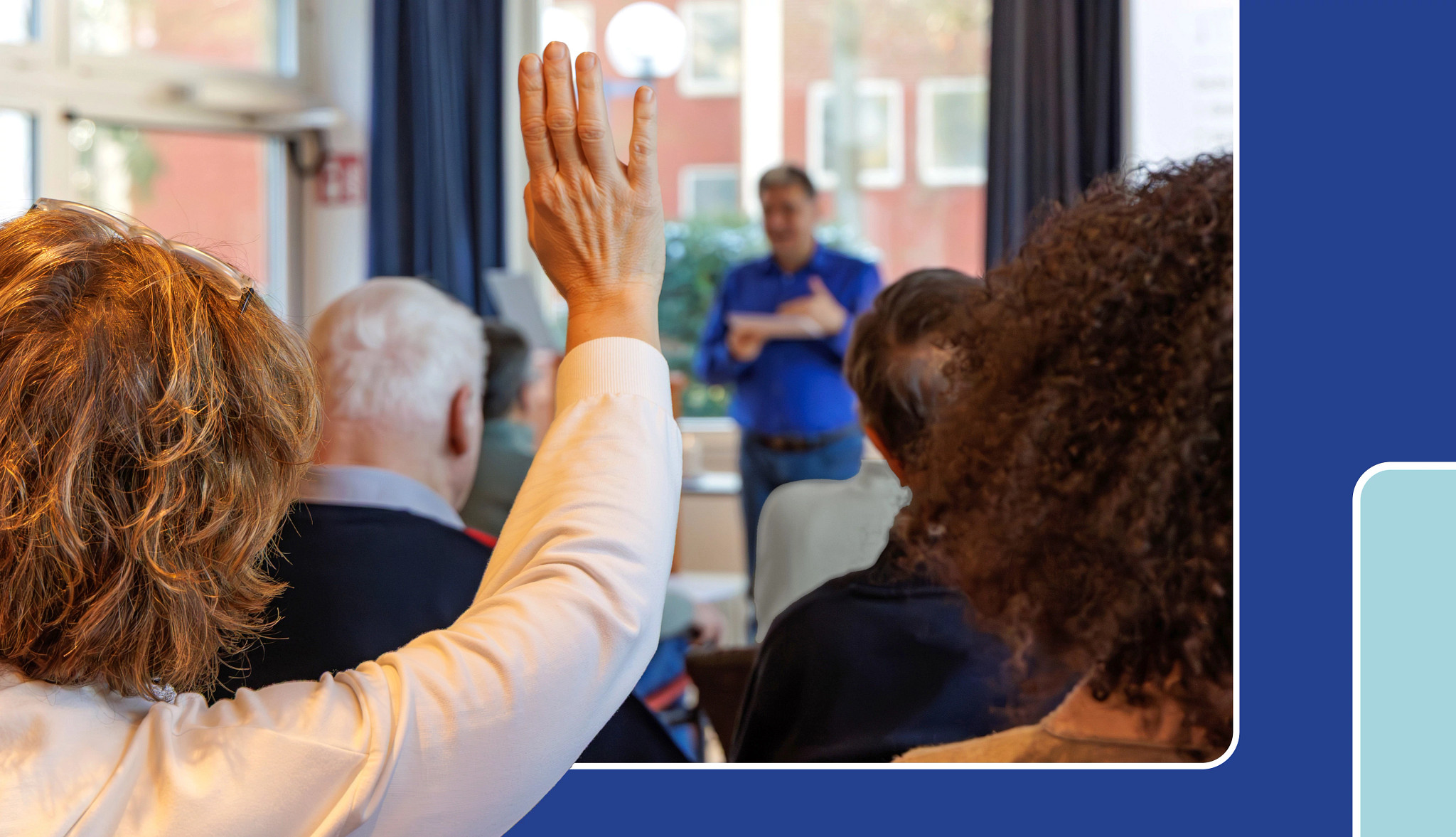 a woman sitting in a group raising her hand as she listens to a man speaking