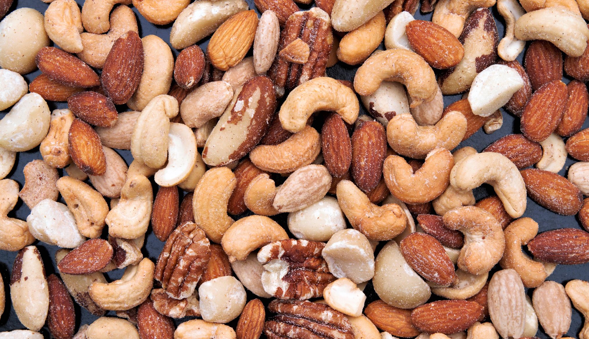 mixed nuts spread out on a dark background