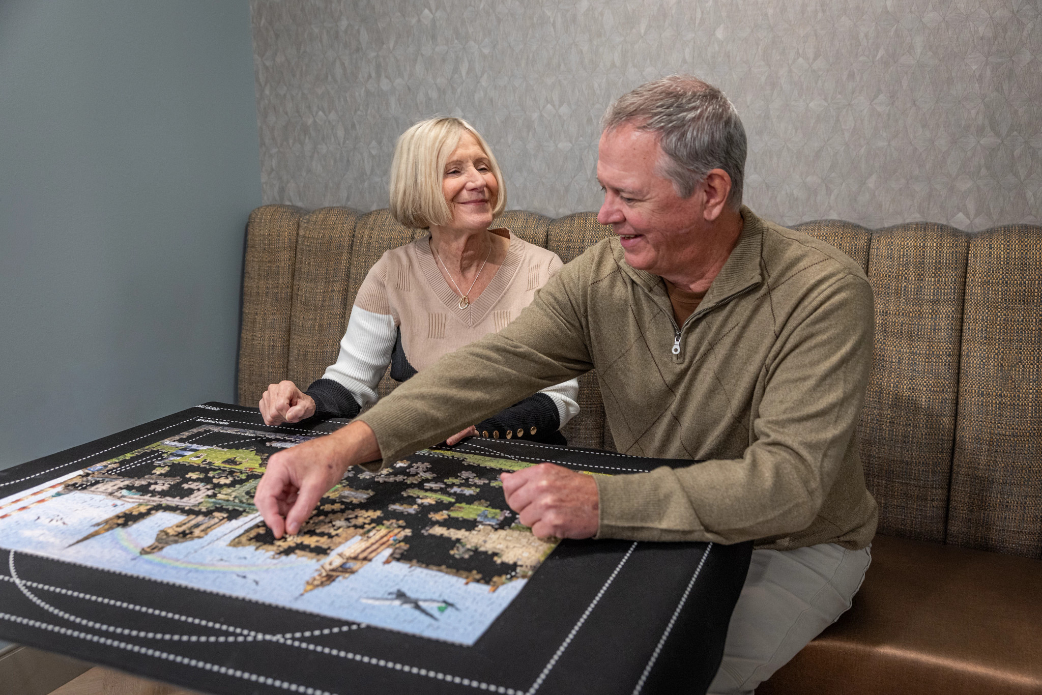 an older woman smiles at a man as they work on a puzzle together
