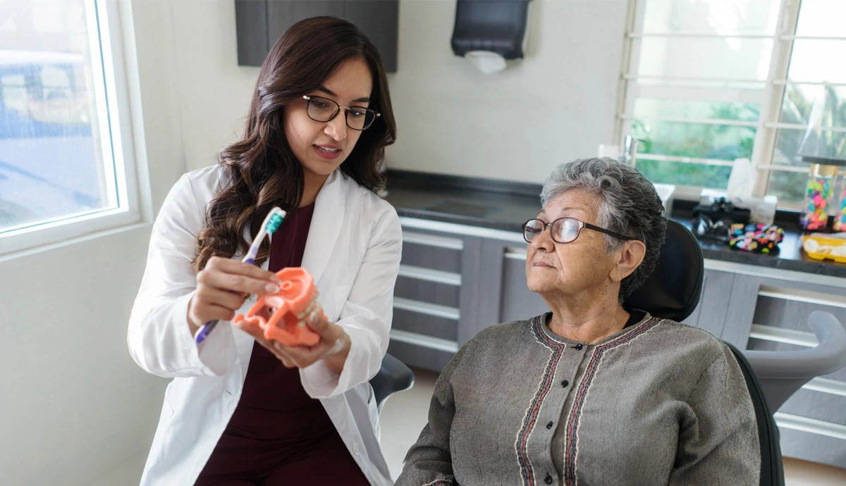 An older woman sitting in a dental chair watching and listening to a dentist speak to her about her teeth and mouth.