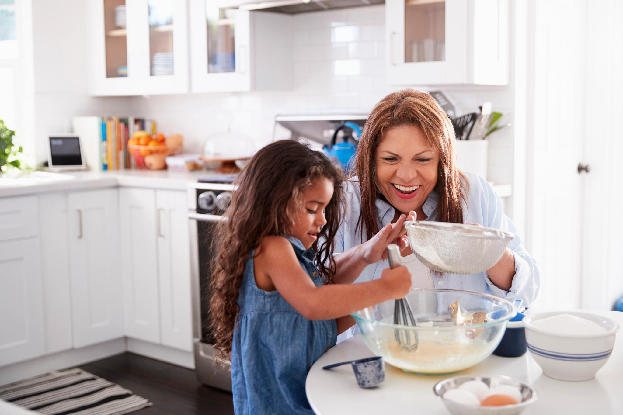 Young Hispanic girl making cake in the kitchen with her grandma, looking down