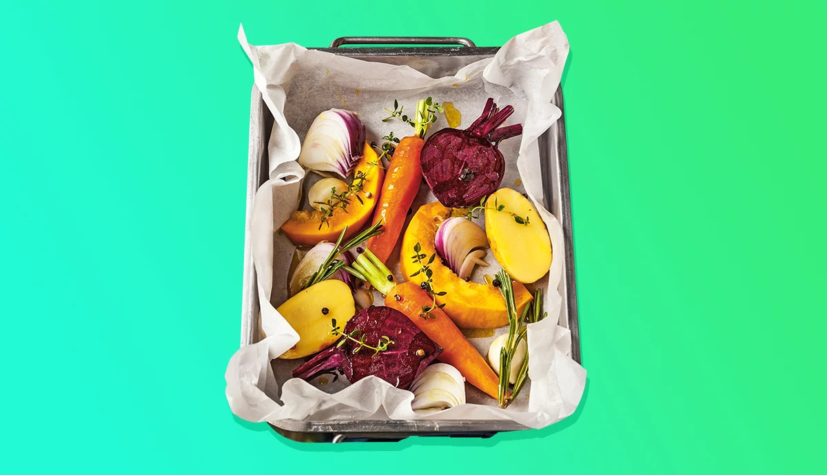 Seasoned root vegetables and fresh herbs arranged on parchment paper in a baking sheet.