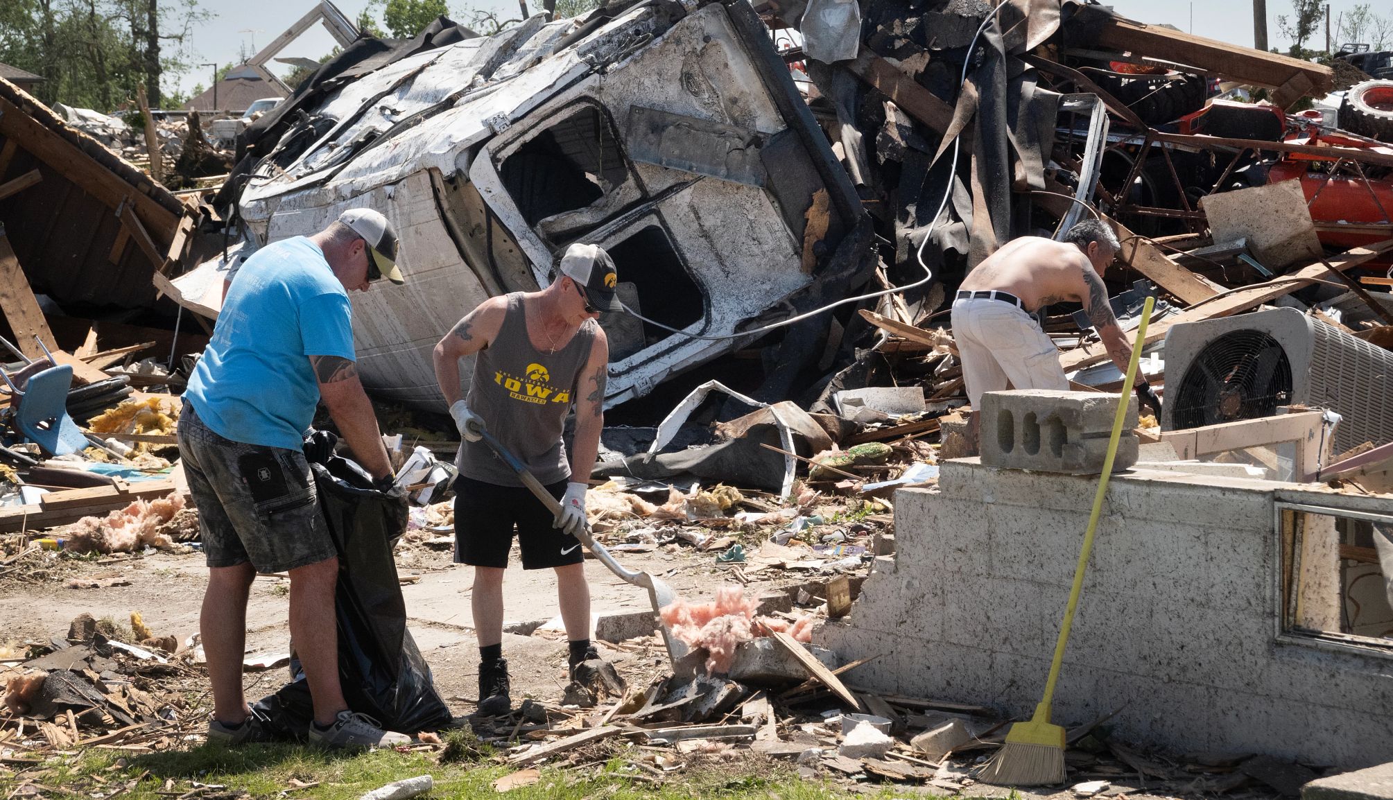 Residentes trabajan en la recuperación y limpieza después de un tornado en Greenfield, Iowa, el 23 de mayo. Un hombre sostiene una bolsa de basura mientras otros dos hombres revisan los escombros durante los esfuerzos de limpieza después de un tornado.
