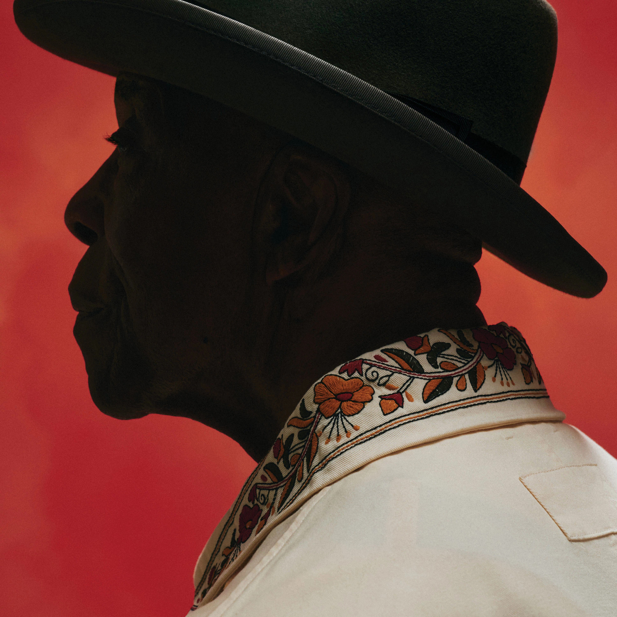 buddy guy posing for a professional portrait in profile, in front of a red background