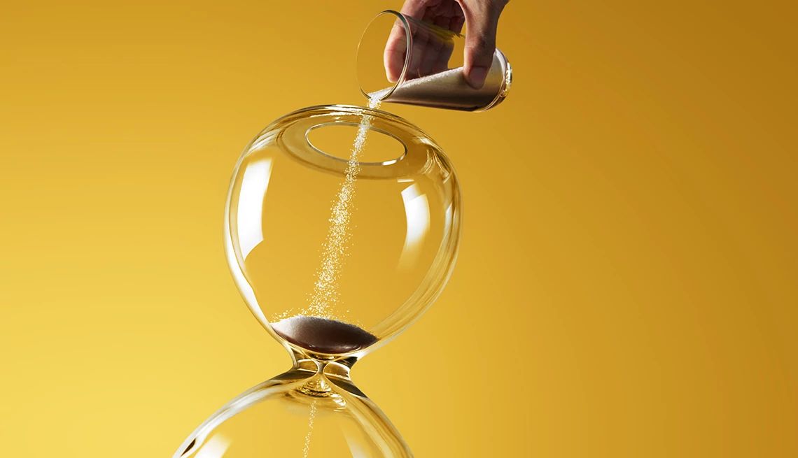 una mano con un vaso de cristal deposita arena en un reloj de arena