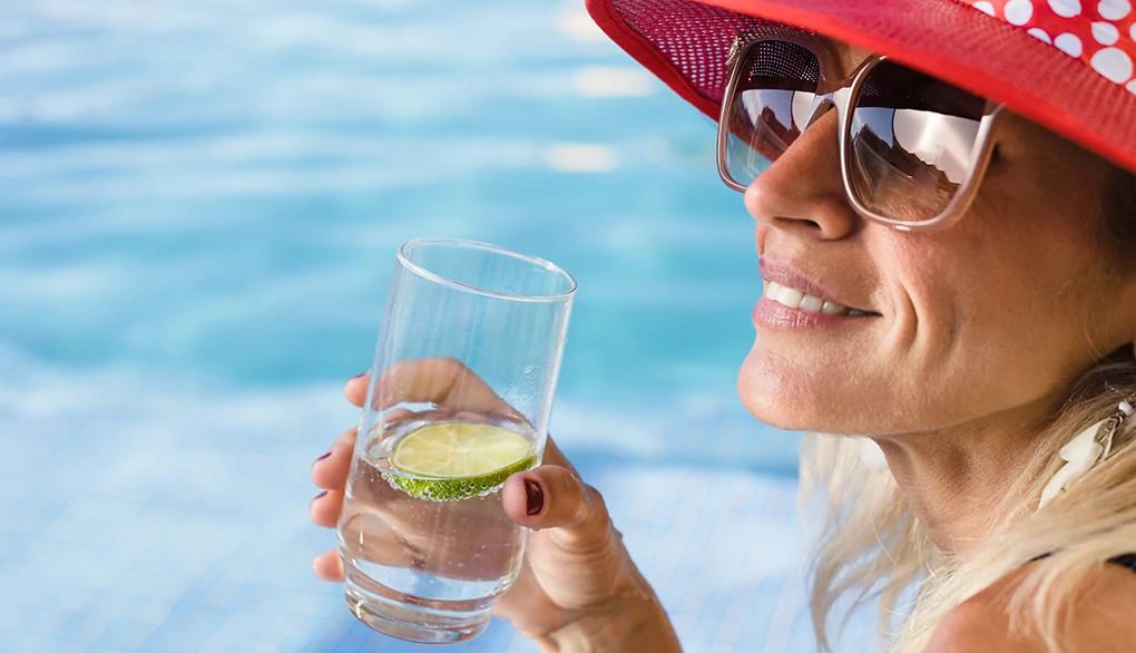 Stay hydrated and support your health by drinking healthier options A woman drinking a glass of water by a pool