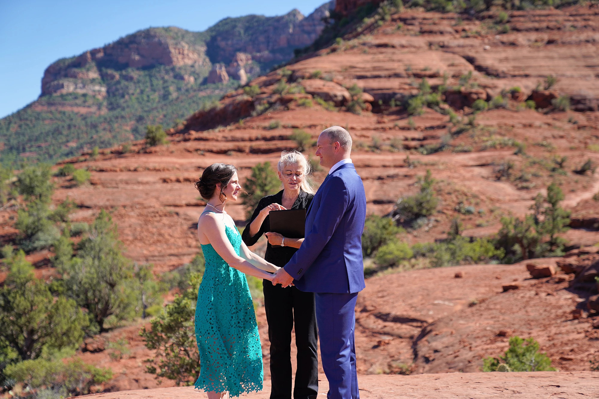 A couple with their officiator standing on red rocks for their private wedding ceremony