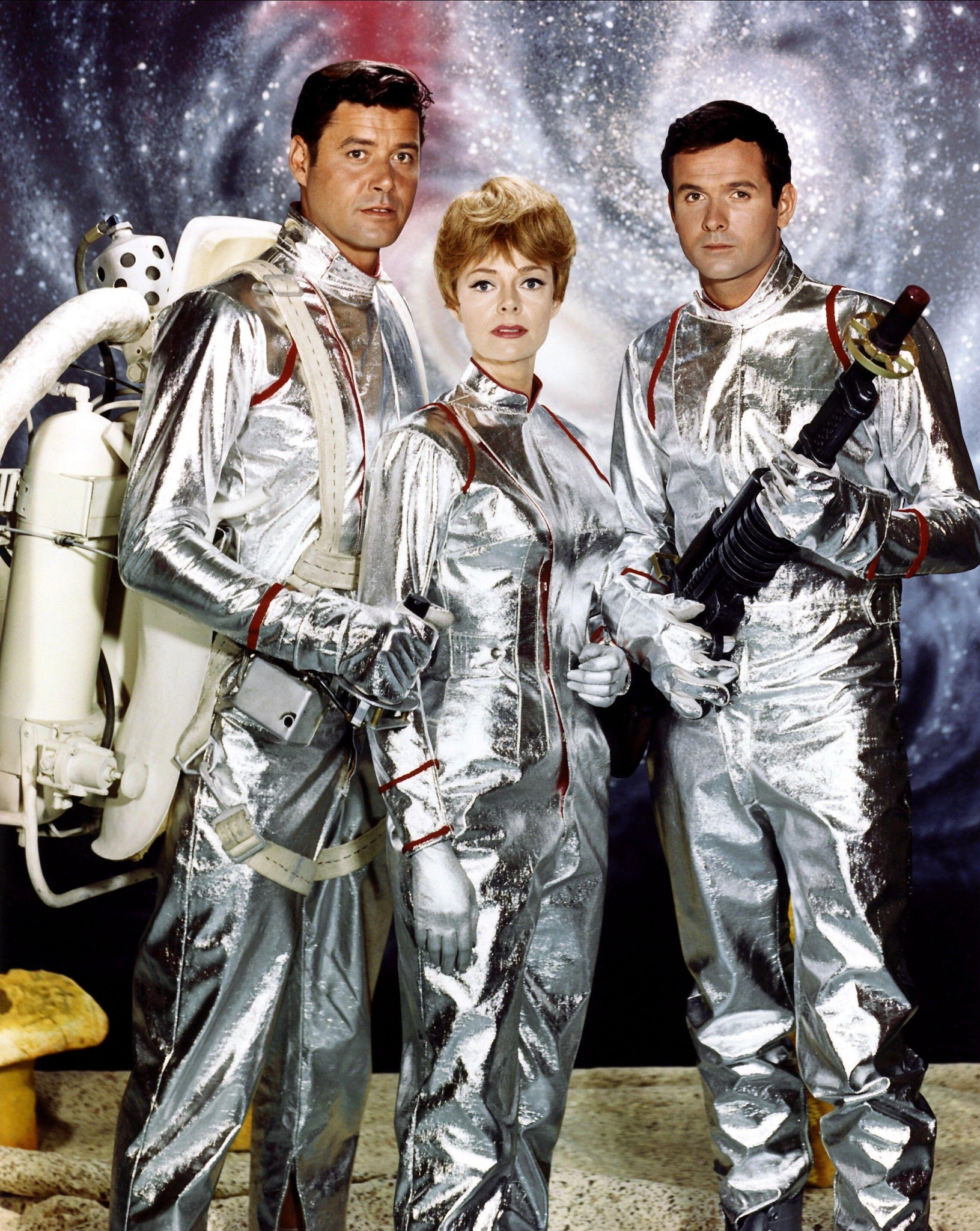 two men and a woman in futuristic space suits. one of the men is holding a futuristic weapon