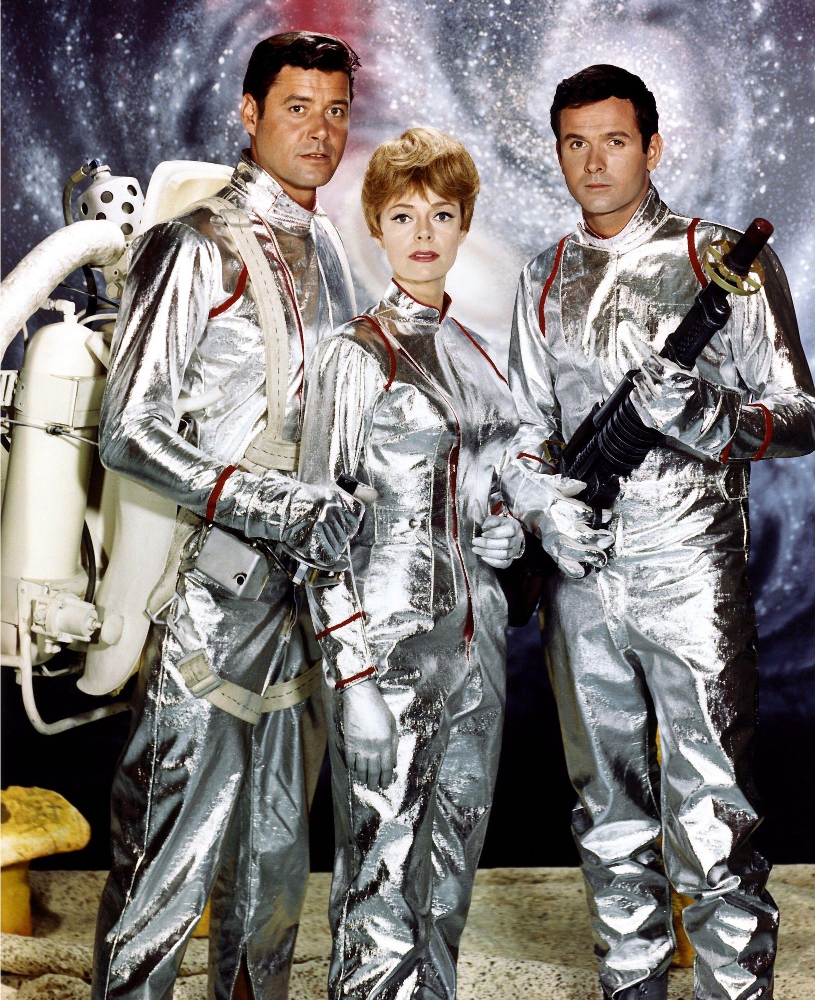 two men and a woman in futuristic space suits. one of the men is holding a futuristic weapon