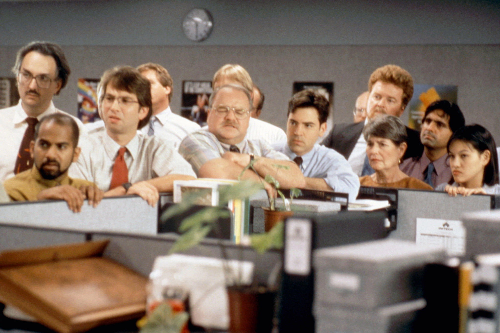 richard riehle crowded around an office cubicle with many other people