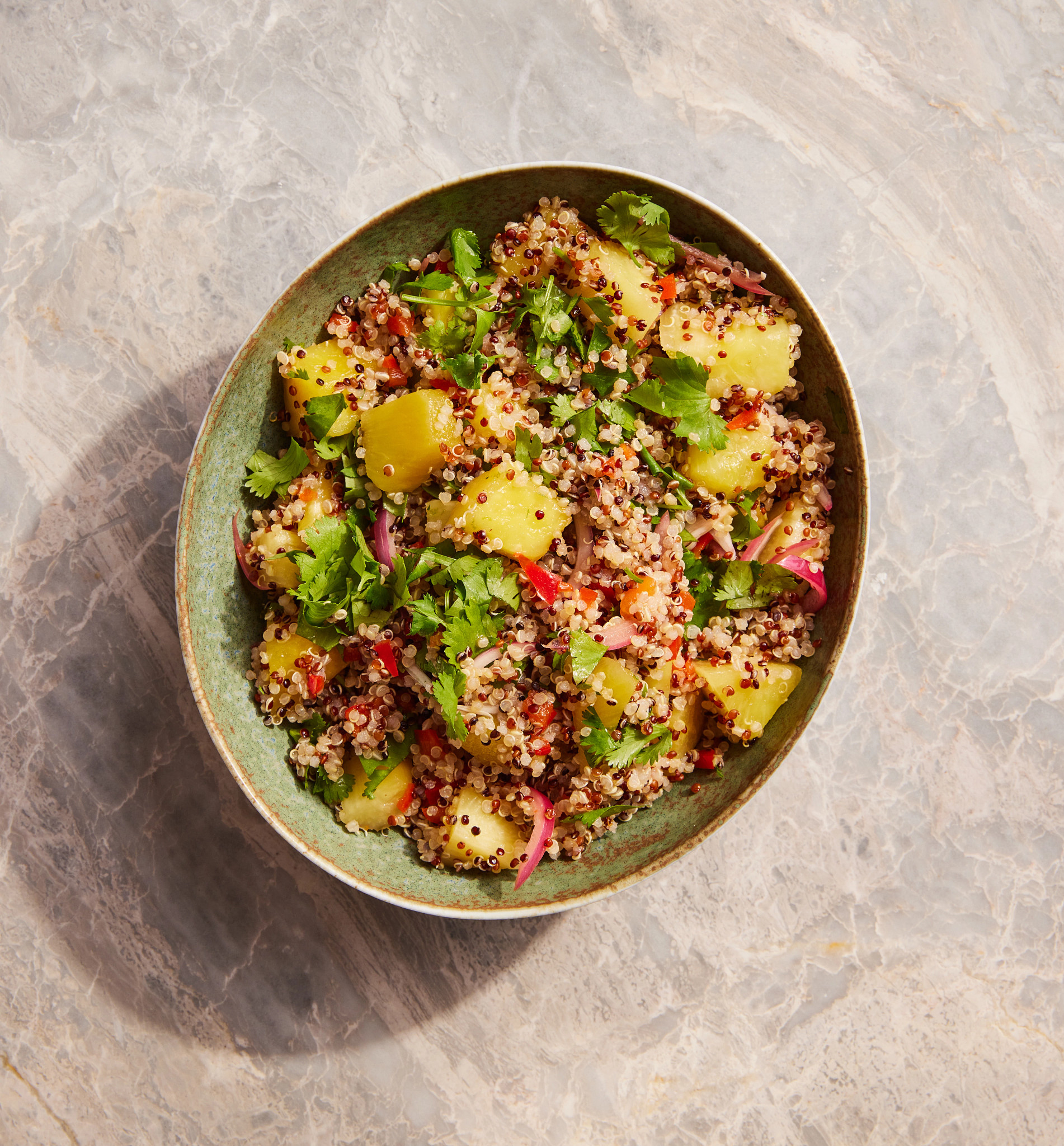 A quinoa salad with pineapple, cilantro and lime is pictured in a bowl atop a countertop.