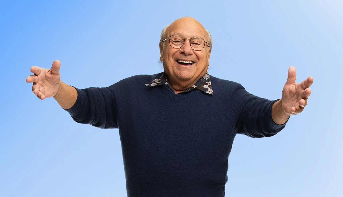 danny devito laughing in a professional portrait, with his arms extended welcomingly