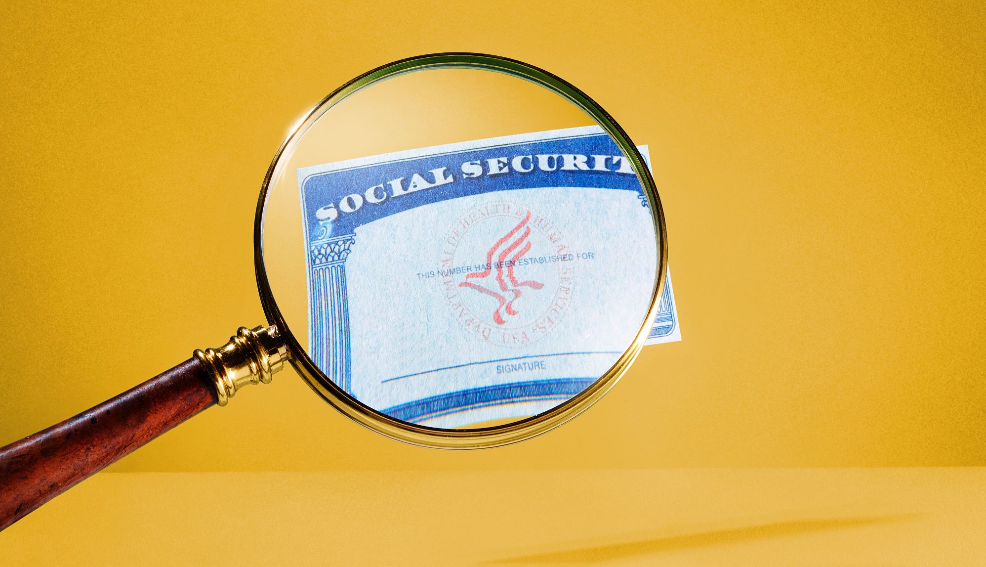 Social Security Report Projects Trust Fund Shortfall social security card under a magnifying glass on a gold background