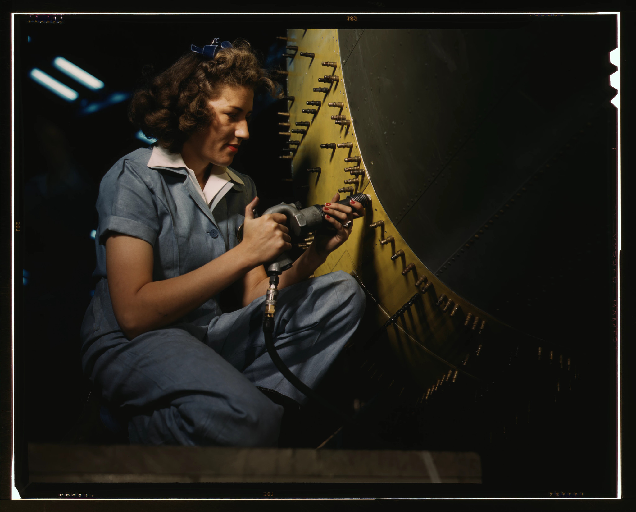 A woman in a blue jumpsuit works on a yellow aircraft.