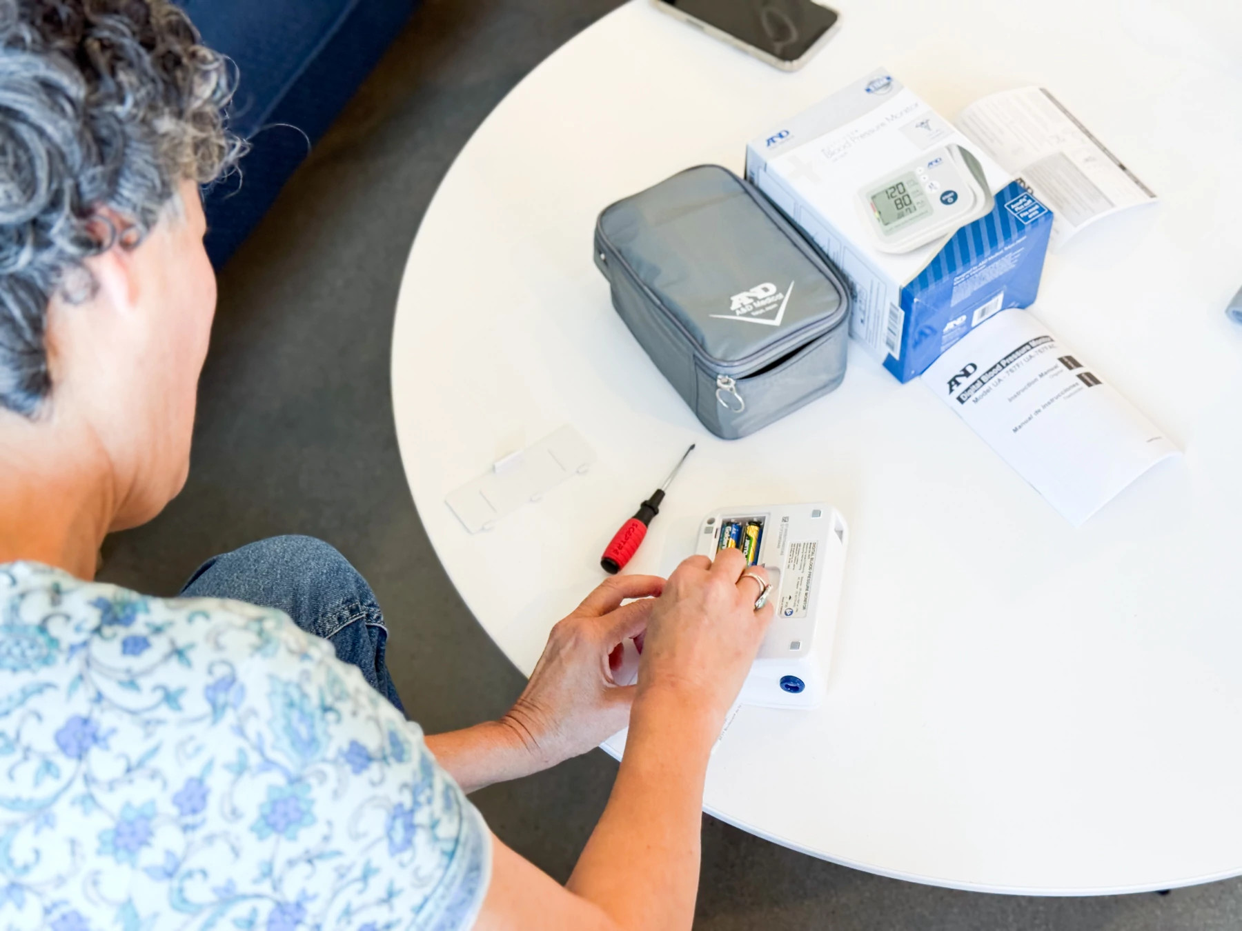 A woman putting the batteries in the A&D Medical Premium Multi-User blood pressure monitor.