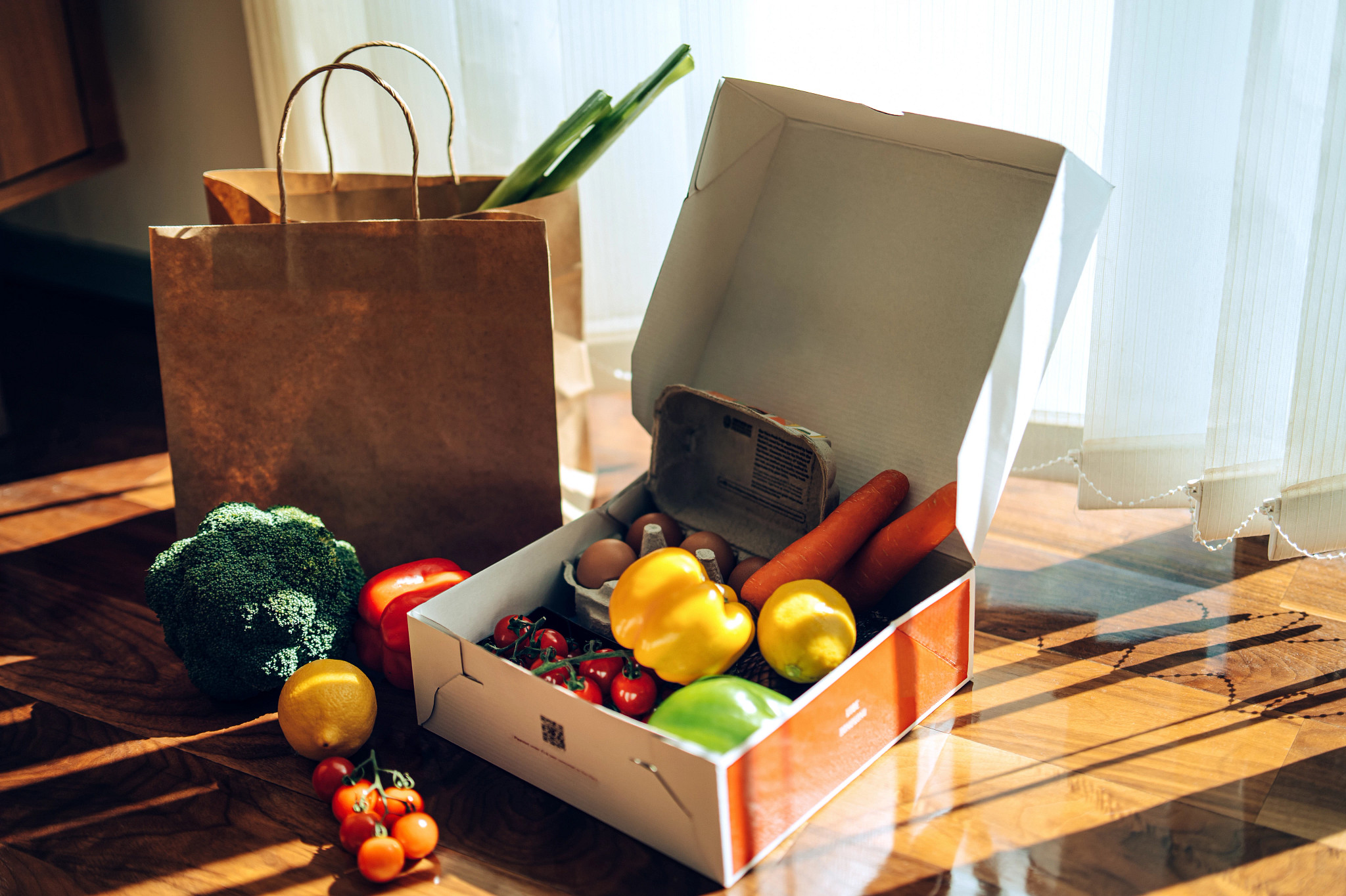 A box and paper bag on a table containing vegetables