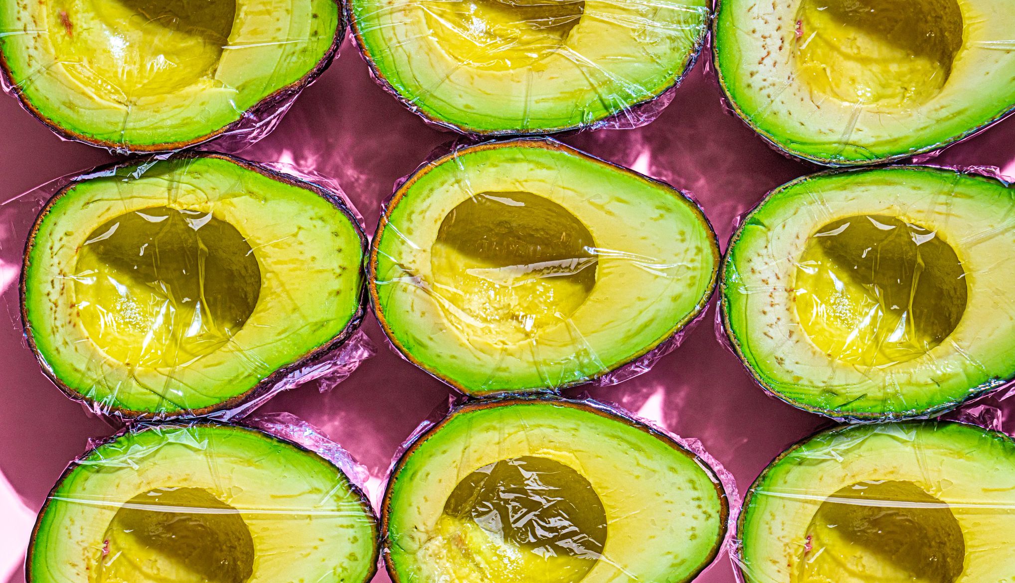 freeze sliced advocado wrapped in plastic wrap sliced avocado on a pink background