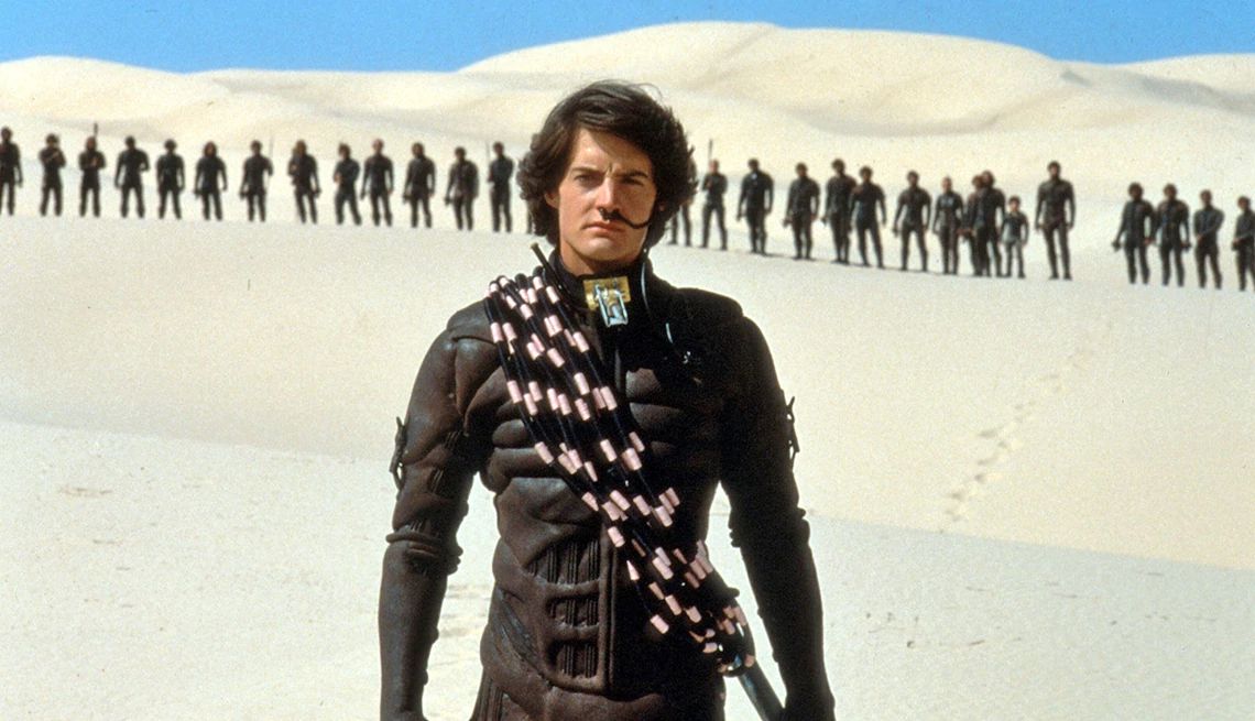 Kyle MacLachlan standing in a desert with people behind him in the horizon in the 1984 film "Dune."