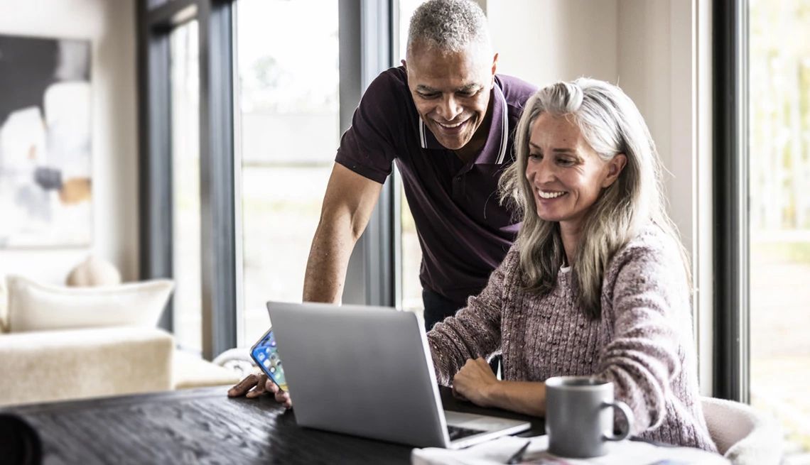 Husband and wife looking at their finances on a laptop at the kitchen table with coffe cup sitting near by