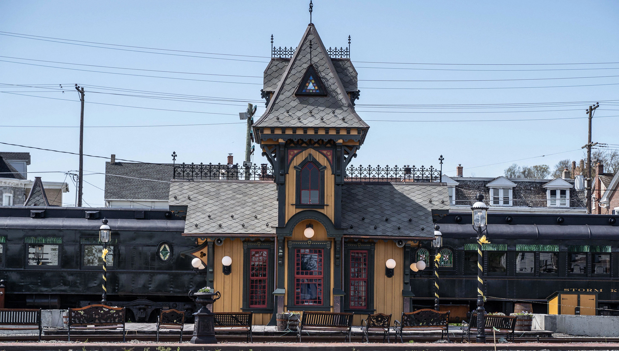 A historic train station with Victorian-style architecture, a decorative tower, and a vintage railcar