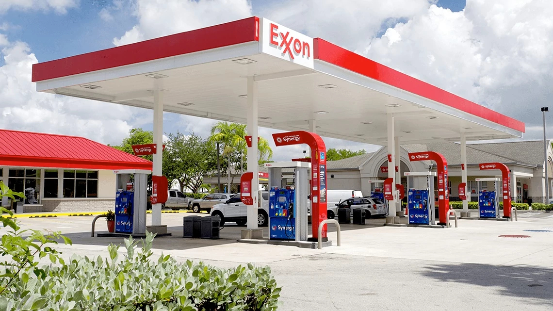 Exxon Mobil gas station with multiple gas pumps, a white car is at one pump, sunny day with white puffy clouds