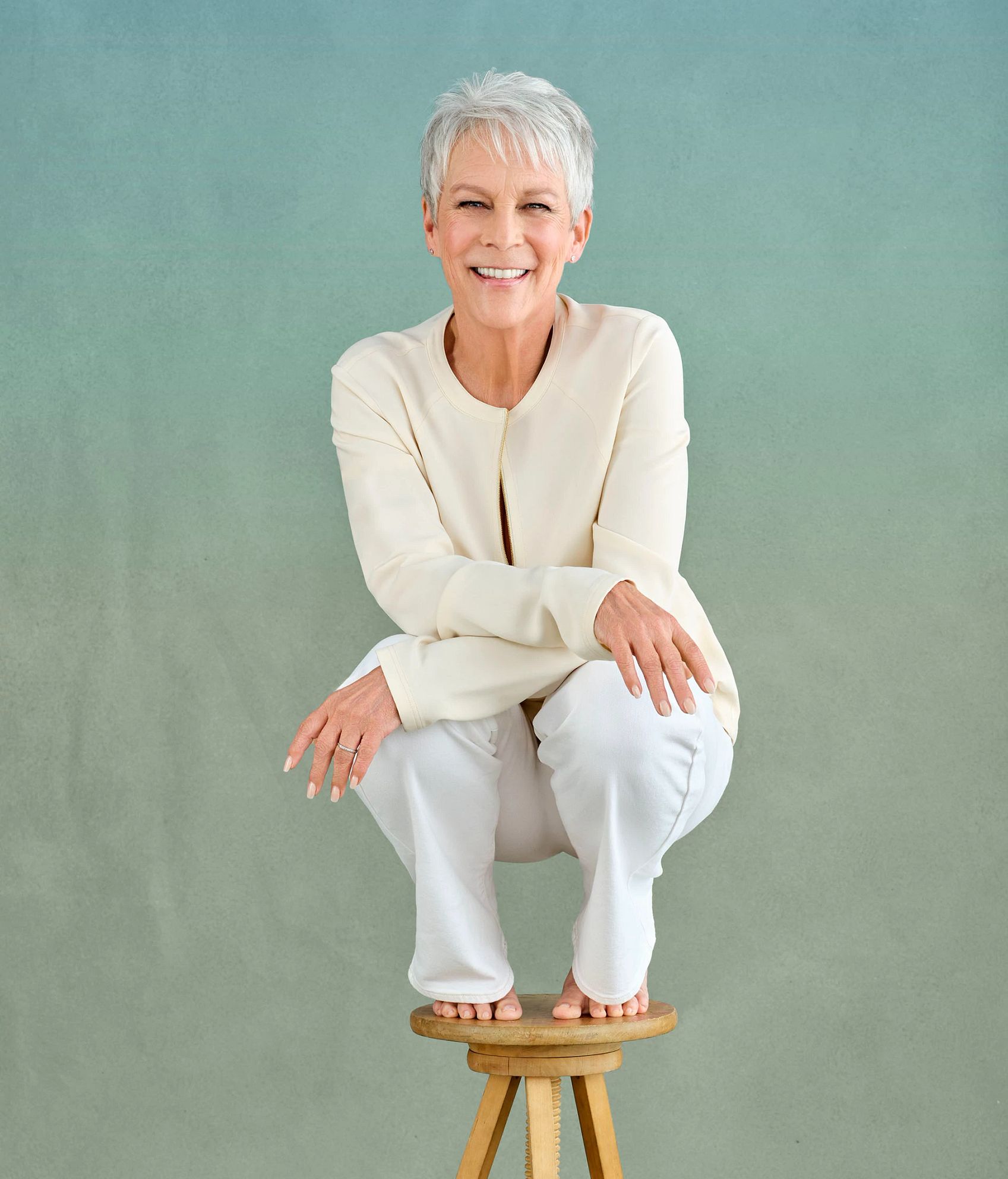 The Liberation of Jamie Lee Curtis jaime lee curtis smiling as she crouches on top of a wooden stool