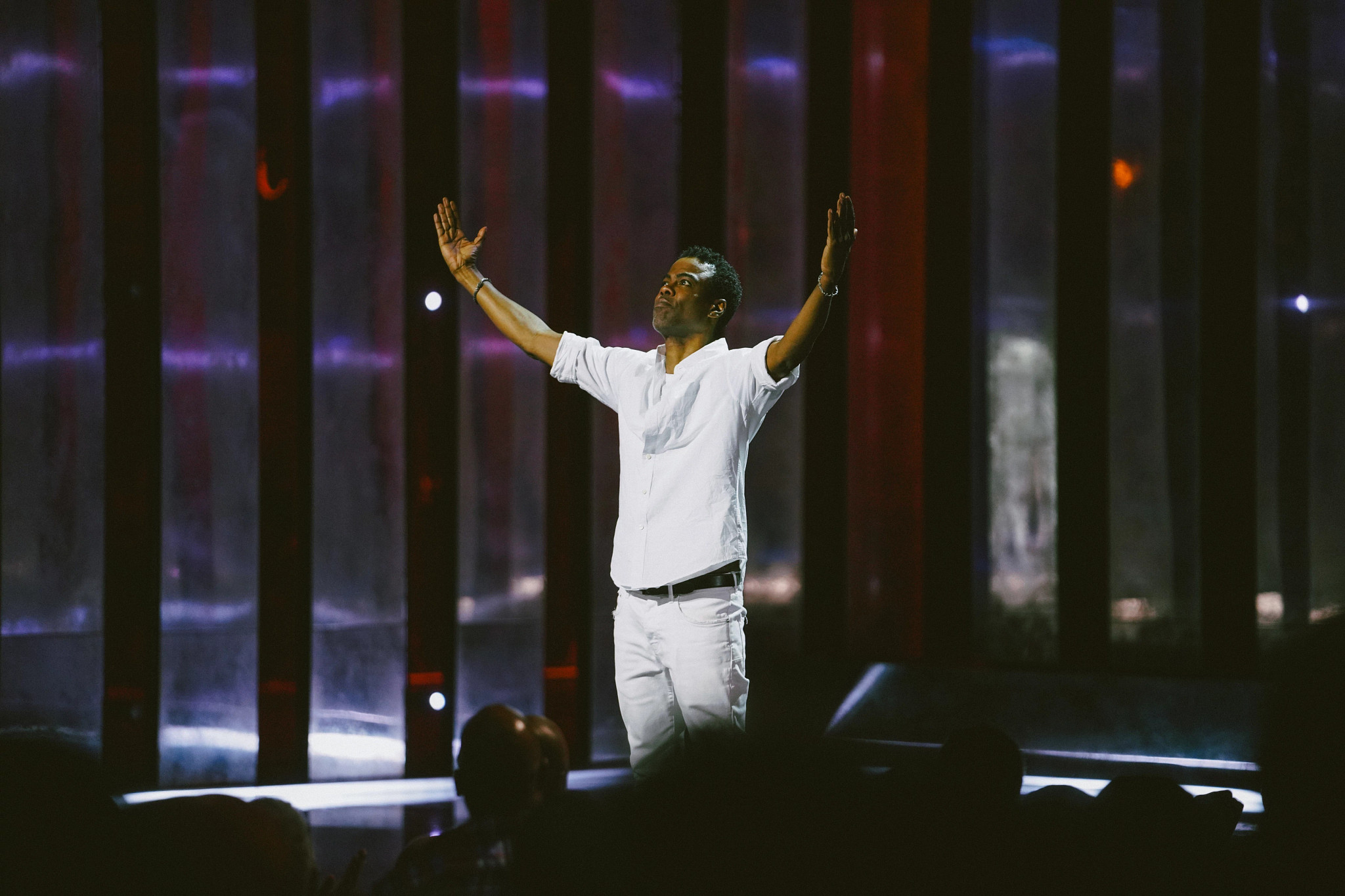 chris rock standing on a stage with his arms outstretched