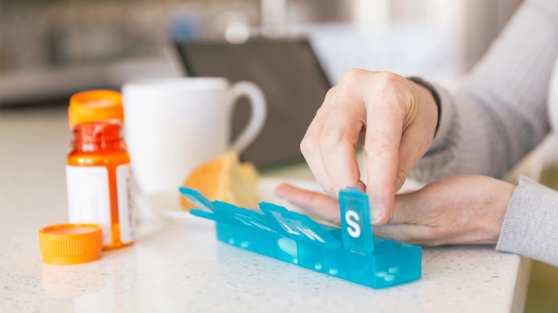 woman's hands placing pills from a bottle to a weekly pill sorter container