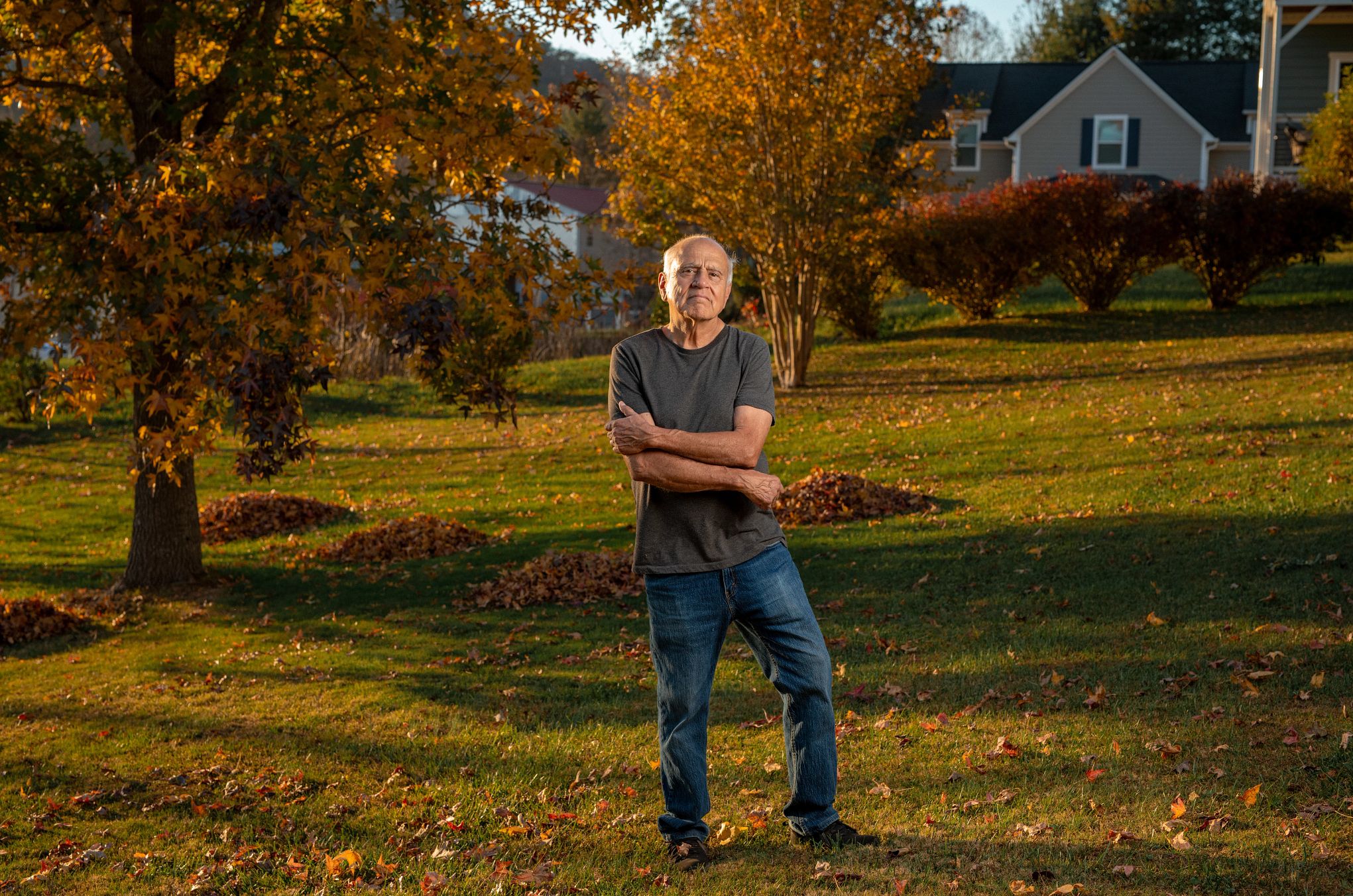 Ed Escalante  a man stands in a yard in front of trees piles of leaves