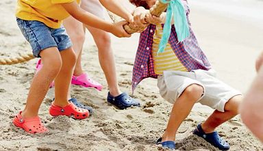 Family wearing Crocs shoes playing tug-of-war on the beach