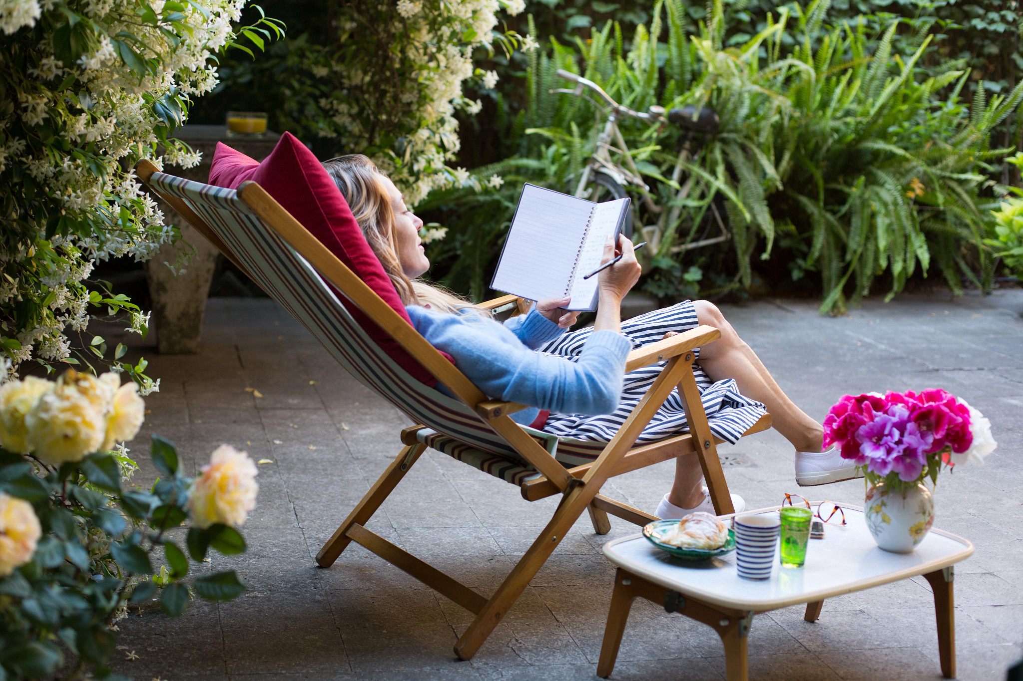 Woman relaxing on deck chair in backyard, reading a notebook while having breakfast