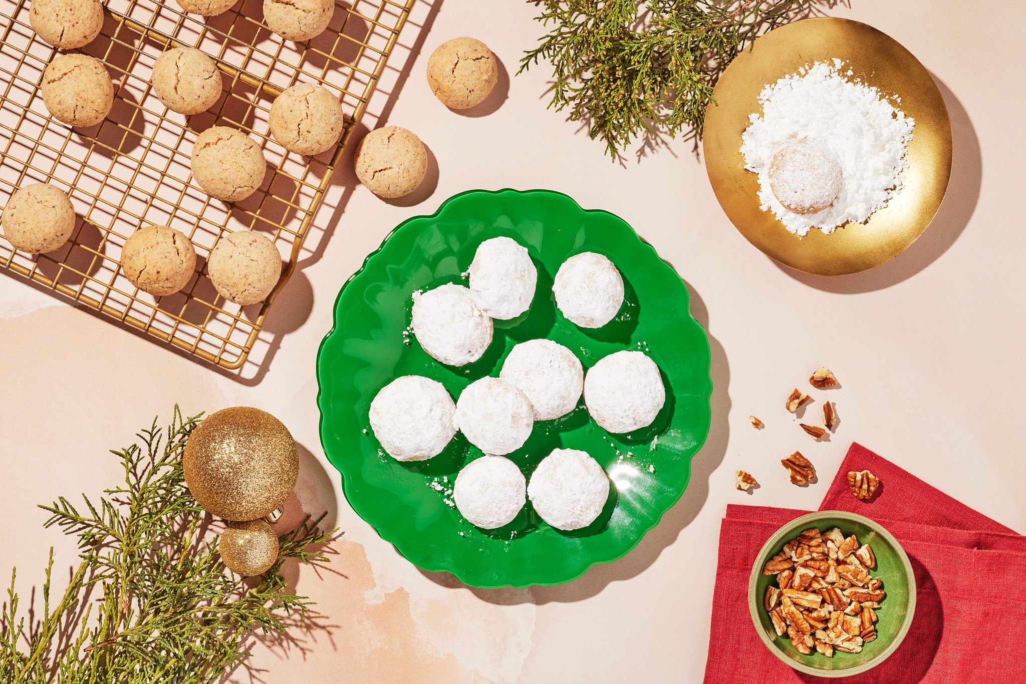Powdered sugar cookies on a green plate beside a cooling rack and holiday decorations