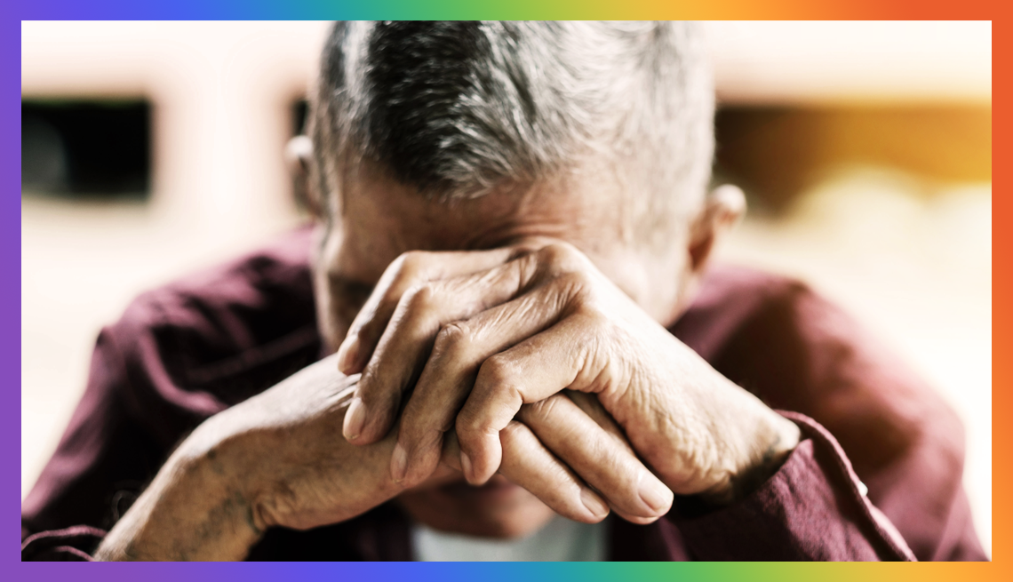 LGBTQ+ Older Adults Worry About Social Isolation a man with his hands clasped against his forehead surrounded by a rainbow border