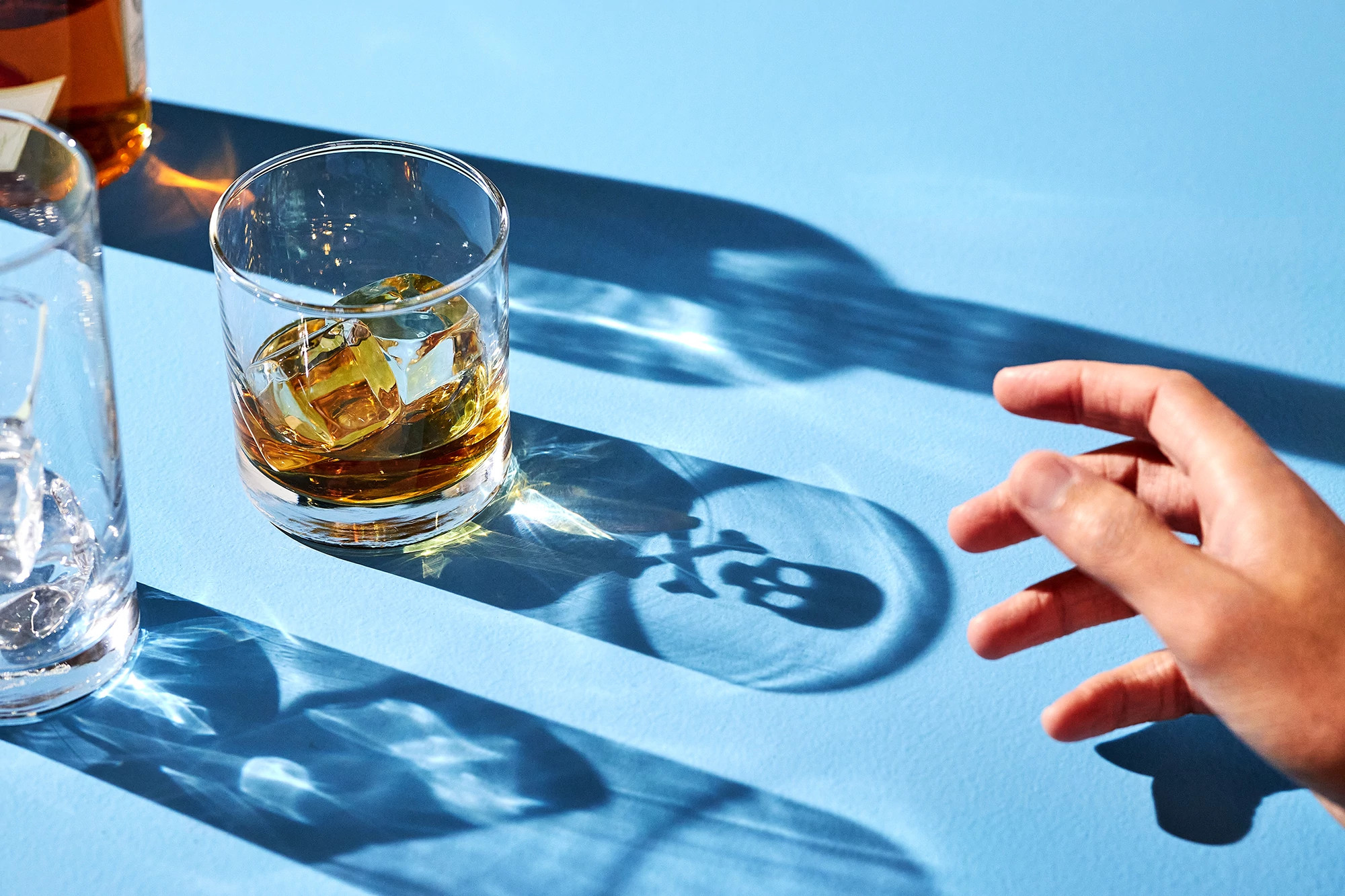 Hand reaching out to alcohol drink with shadow of skull and cross bones