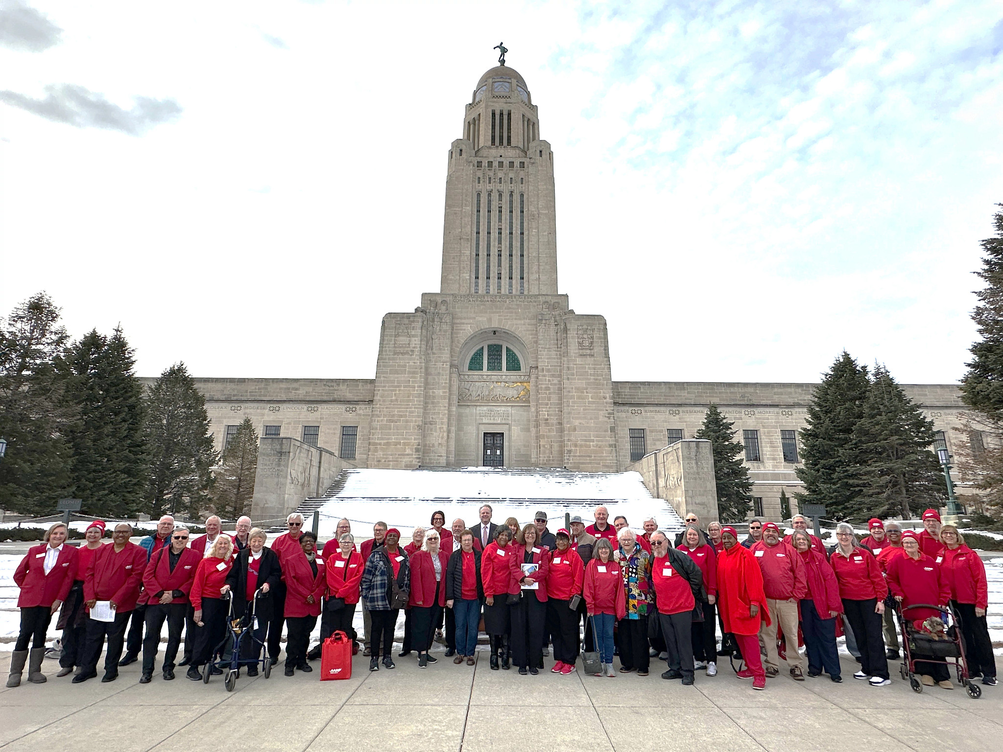 A group of AARP volunteers wearing red pose outside the Nebraska State Capitol on a snowy day
